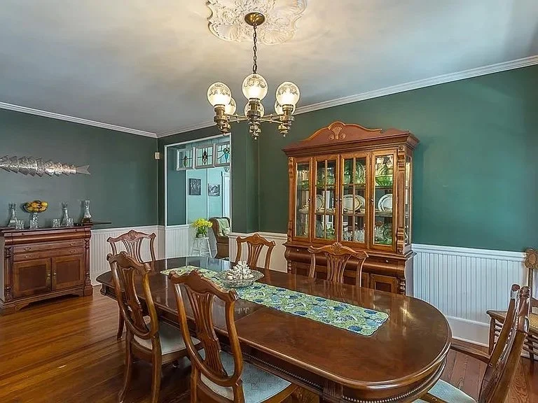 Dining room with green walls, wooden dining table with six chairs, a glass-fronted china cabinet, a sideboard, and a chandelier with five globes hanging from the ceiling.