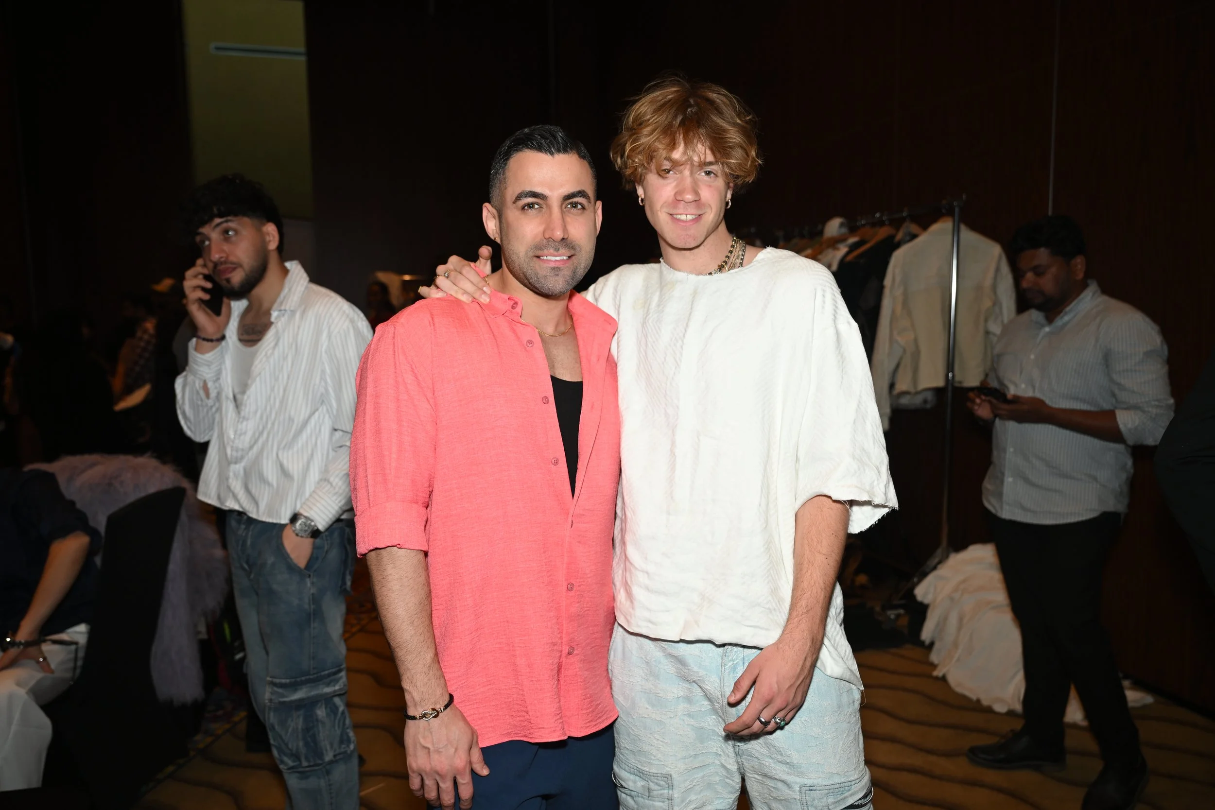 Two men standing together and smiling at a social event, with other people in the background.