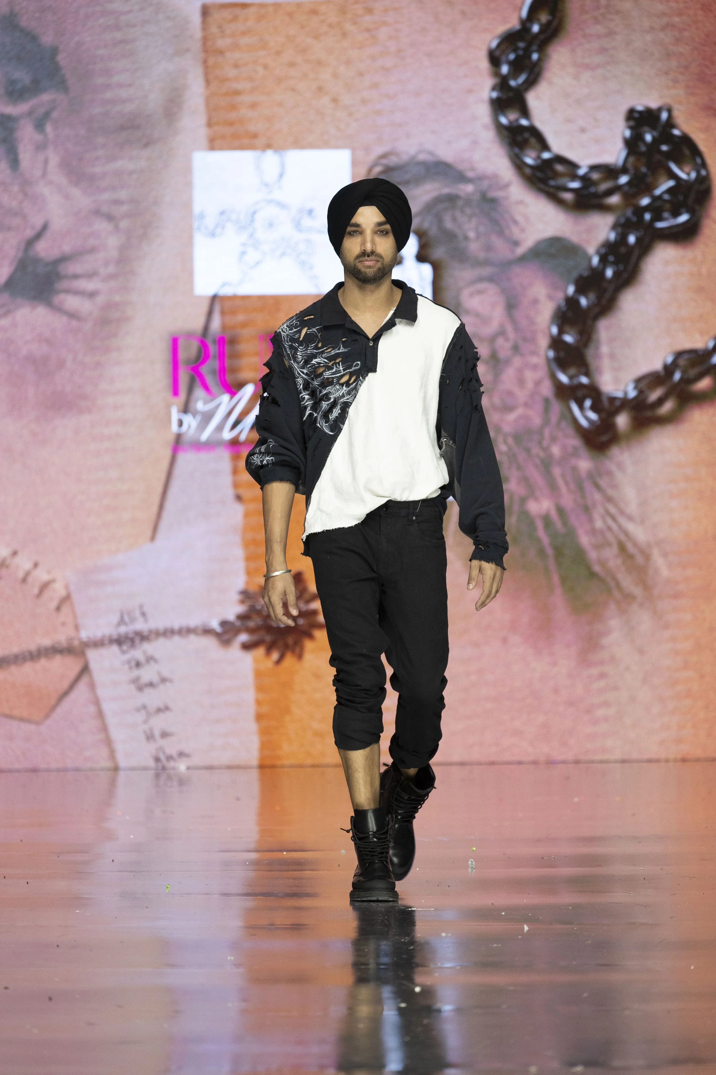 Male model walking on runway with pink and orange background featuring a black chain and abstract images.