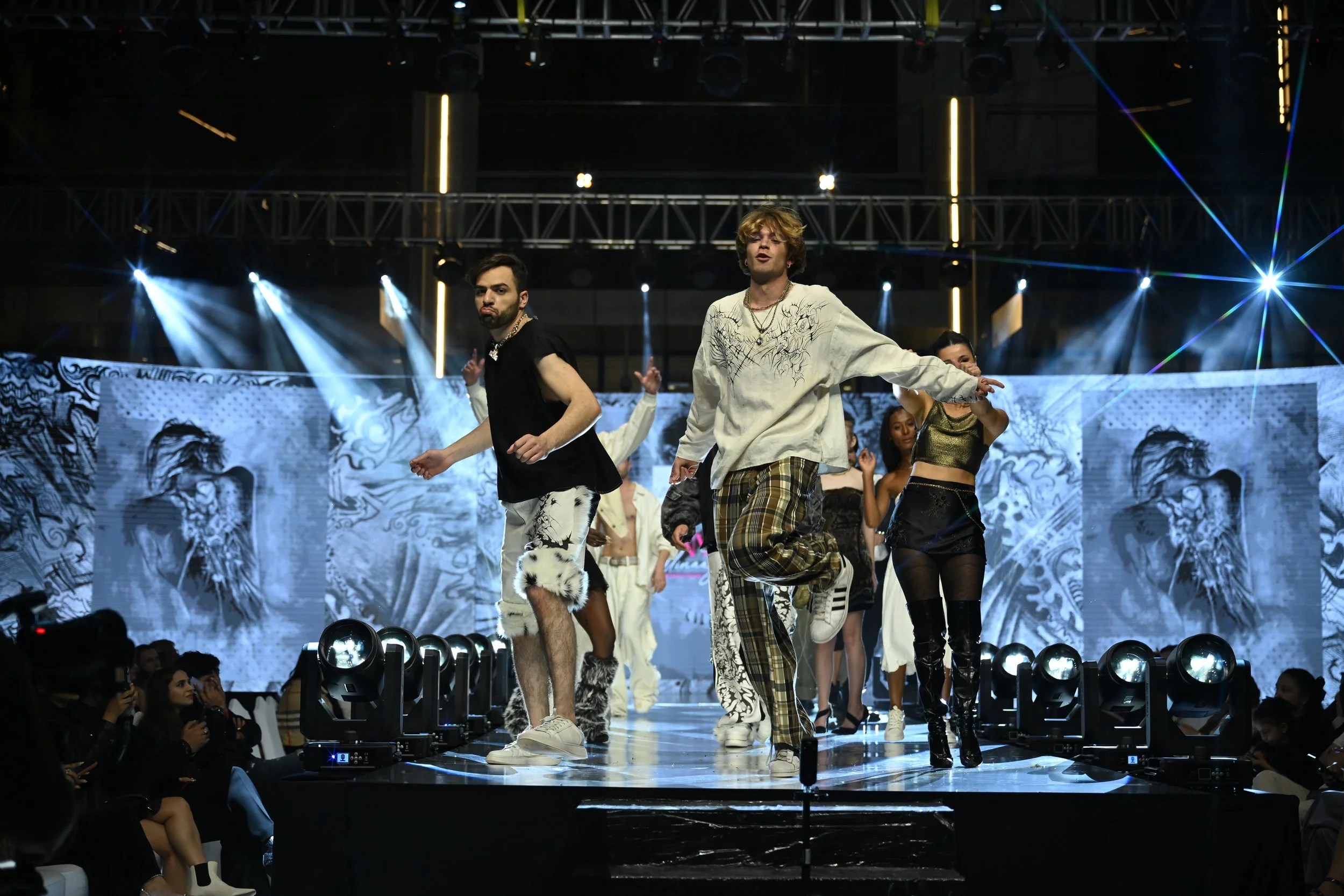 Group of fashion models walking on runway during a fashion show with bright stage lights and digital backdrop