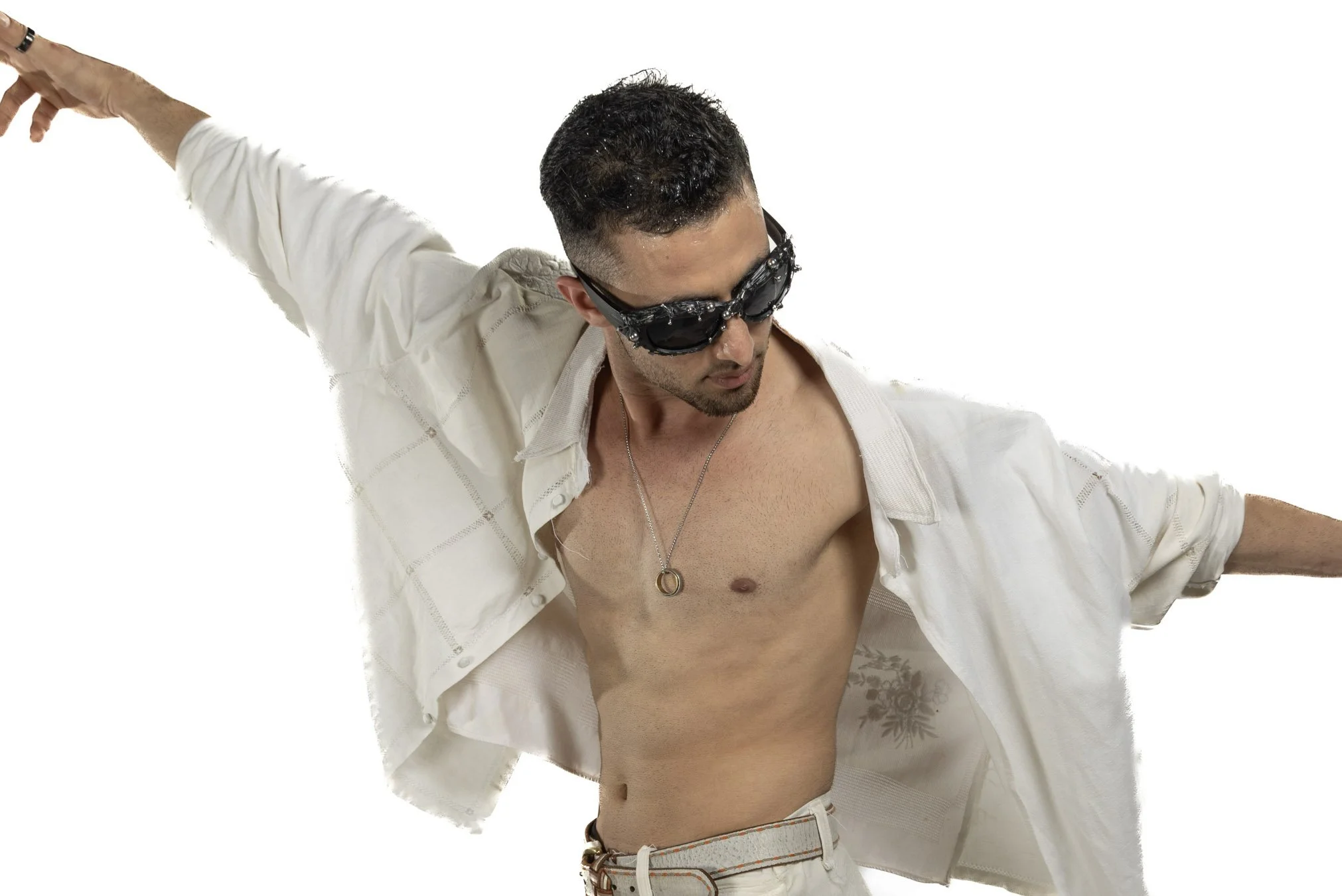 Young man in sunglasses with open white shirt, revealing chest and torso, posing with arms extended, against a plain white background.