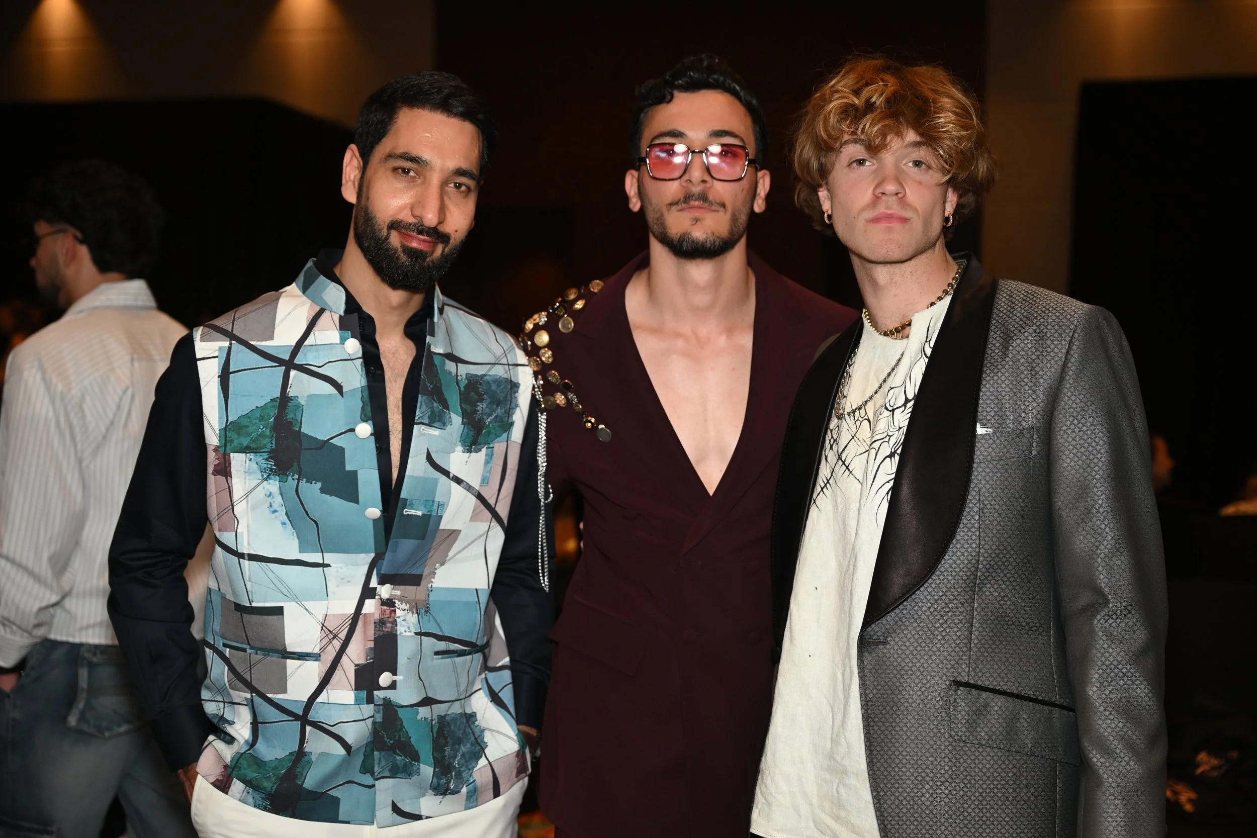Three men in fashionable attire standing together at an indoor event.
