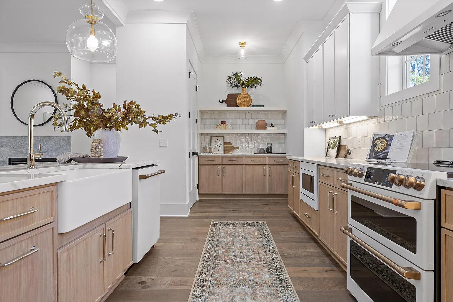 A modern kitchen with wood cabinets, white countertops, a white farmhouse sink, a white stove, and open shelves with decorative items and plants.