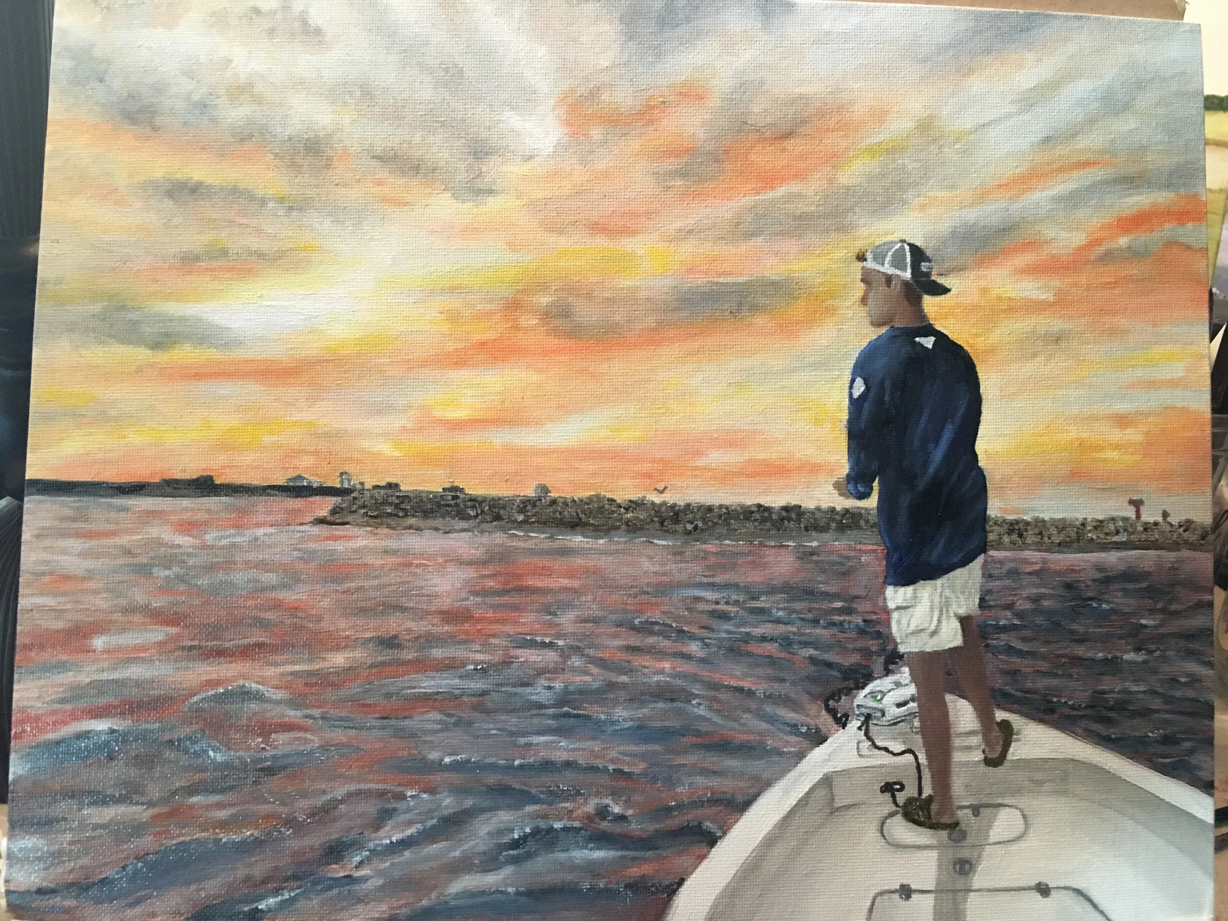 A painting of a young man fishing from a boat at sunset. The sky is filled with orange, yellow, and gray clouds. The man is wearing a navy blue sweatshirt, white shorts, and a cap, standing on the boat's bow with a fishing rod in hand, facing the wat
