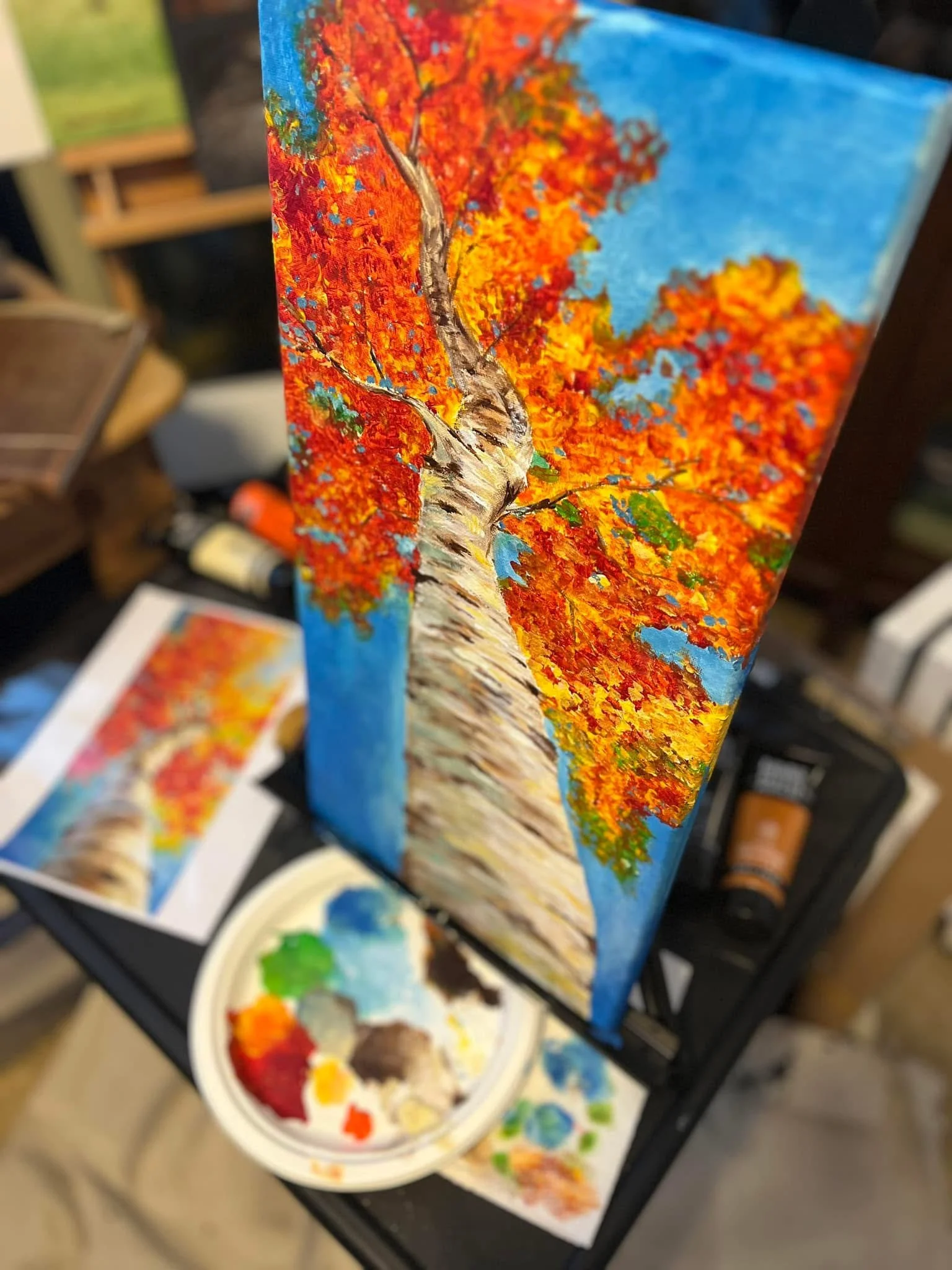 An oil painting of a tree with orange and red autumn leaves on a blue sky background, depicting a textured birch trunk.