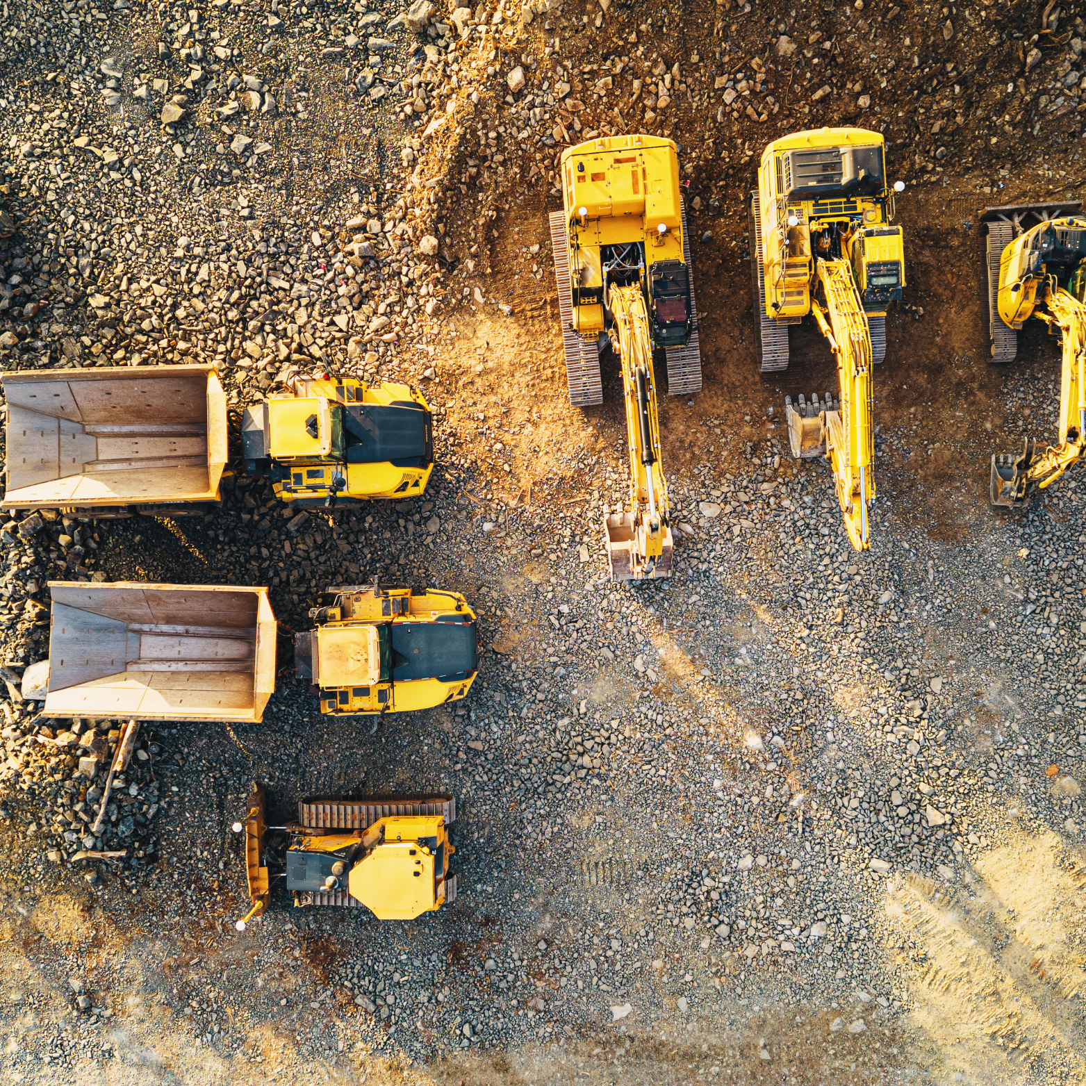 Top-down view of construction vehicles on a rocky site, including excavators and dump trucks.