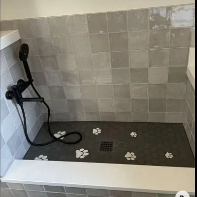 Walk-in shower with light gray tiled walls, a black handheld showerhead, and paw print designs on dark gray flooring