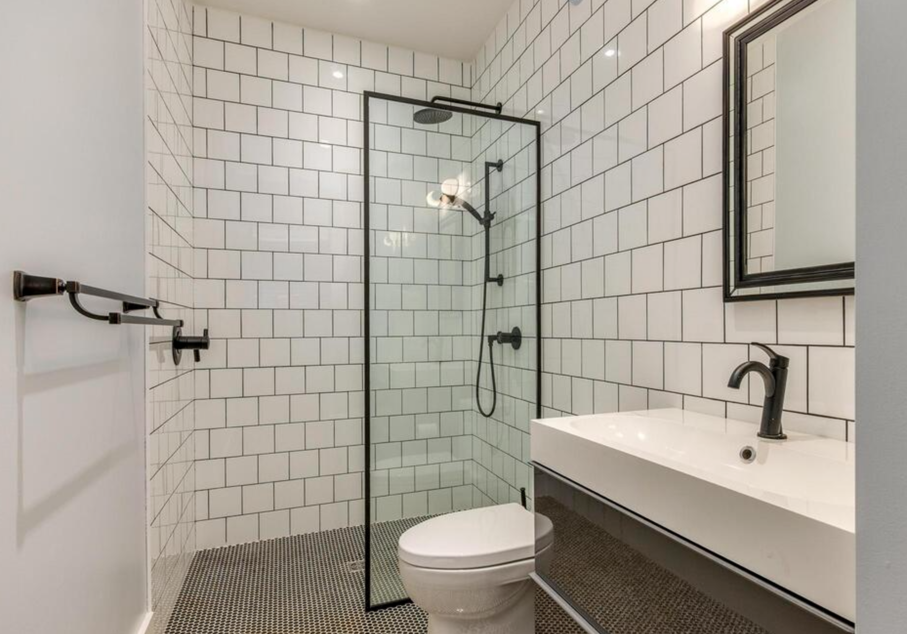 Modern bathroom with walk-in shower, white subway tile walls, black fixtures, and a white rectangular sink with a black faucet.