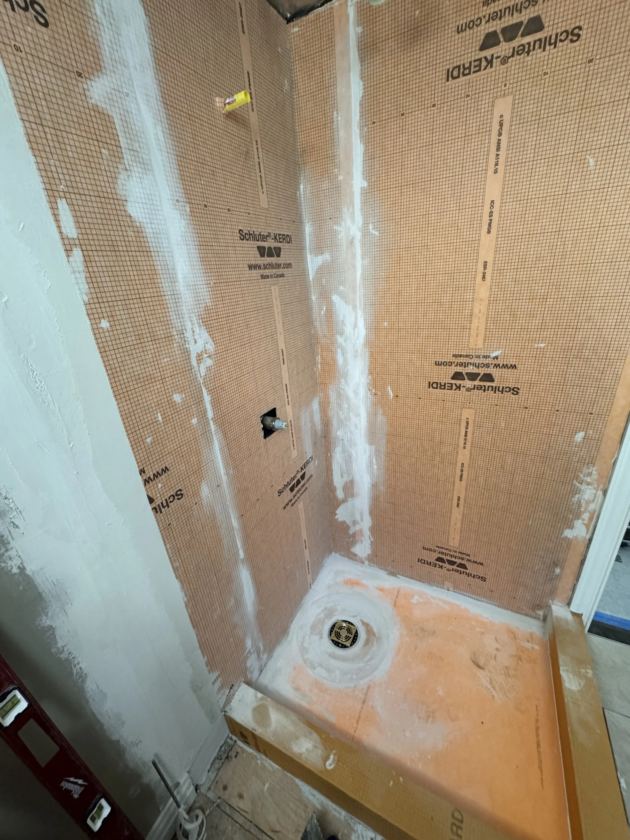 Bathroom shower area under construction with drywall and floor tiles, drain installed, and some drywall mud applied. Schluter Kerdi waterproofing installation Halifax, Dartmouth, Bedford, Lower Sackville, Hammonds Plains, Fall River, Timberlea