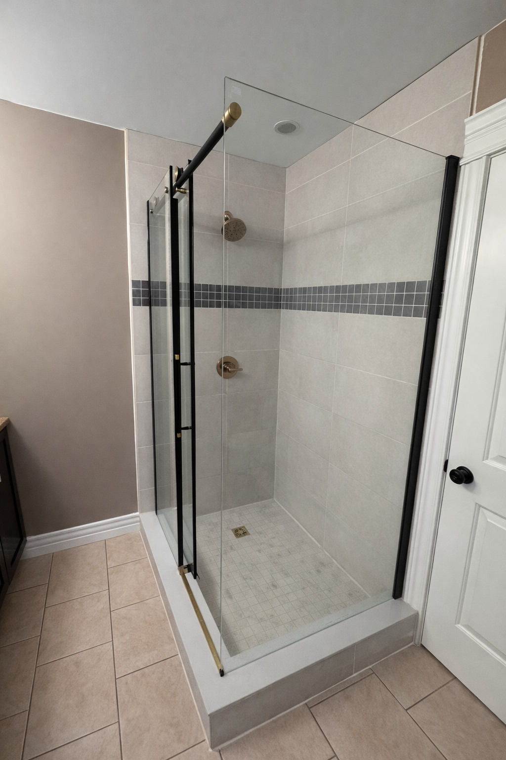 Empty glass shower enclosure with black hardware, beige tiled walls with a black tile border, and a white shower base with small square tiles. Shower Replacement Halifax, Dartmouth, Bedford, Lower Sackville, Hammonds Plains, Fall River, Timberlea