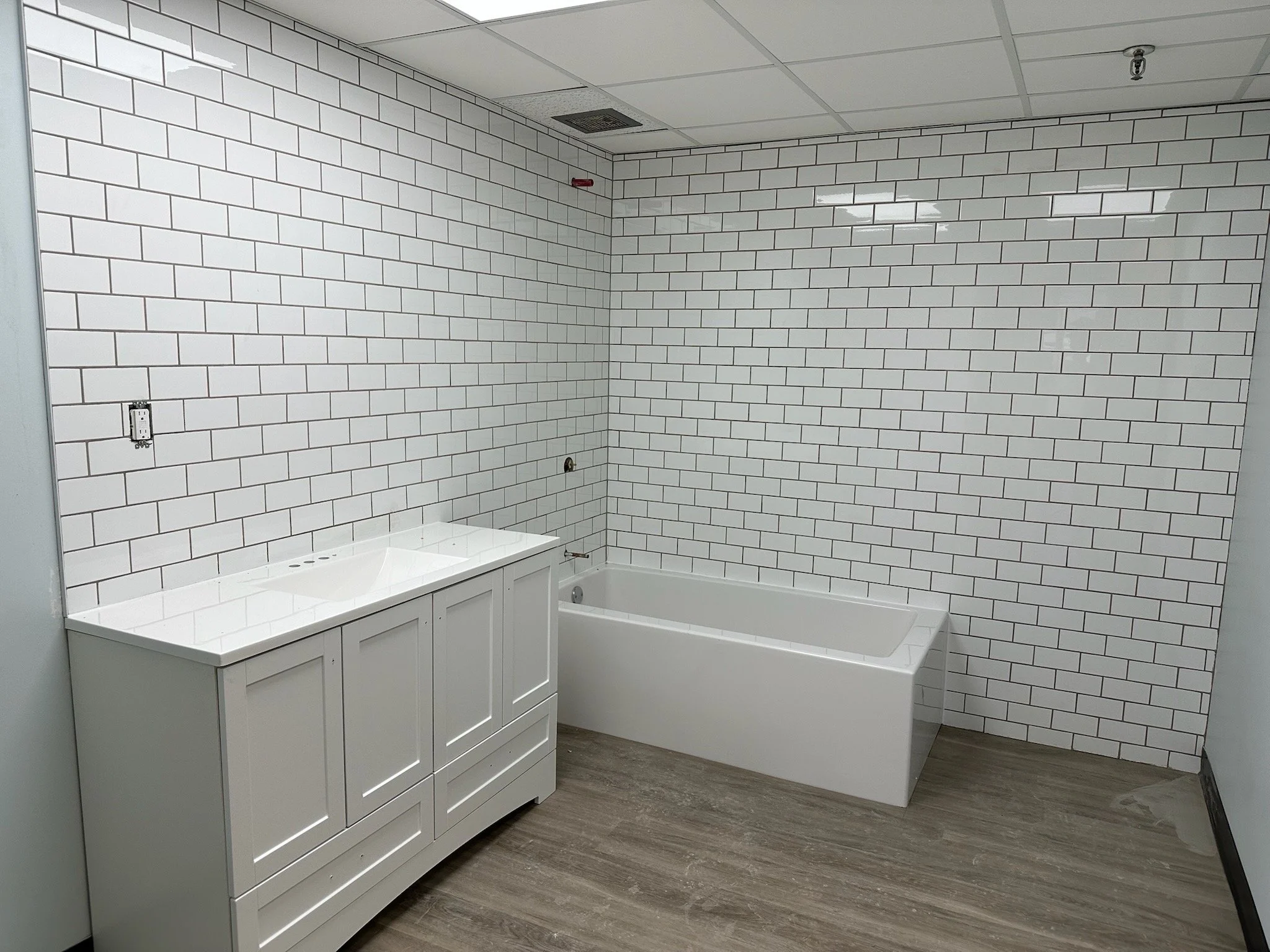 Bathroom with white subway tile walls, a white vanity with a sink, a bathtub, and a ceiling with a vent, appearing to be in an unfinished or newly renovated state.