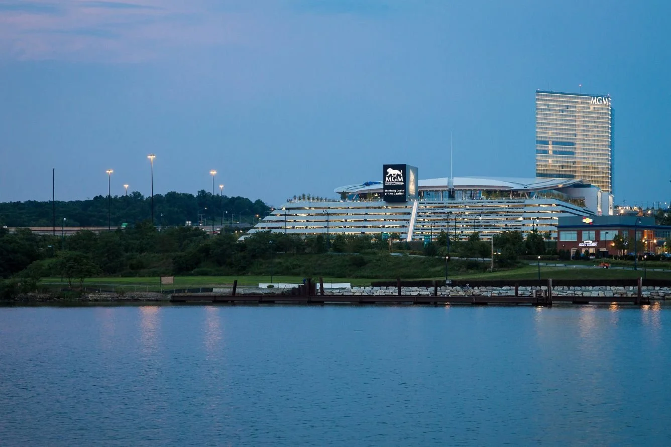 View of a large modern hotel with the MGM logo on a digital sign and a tall building with 'MGM' on the top. The hotel is situated near a body of water at dusk.