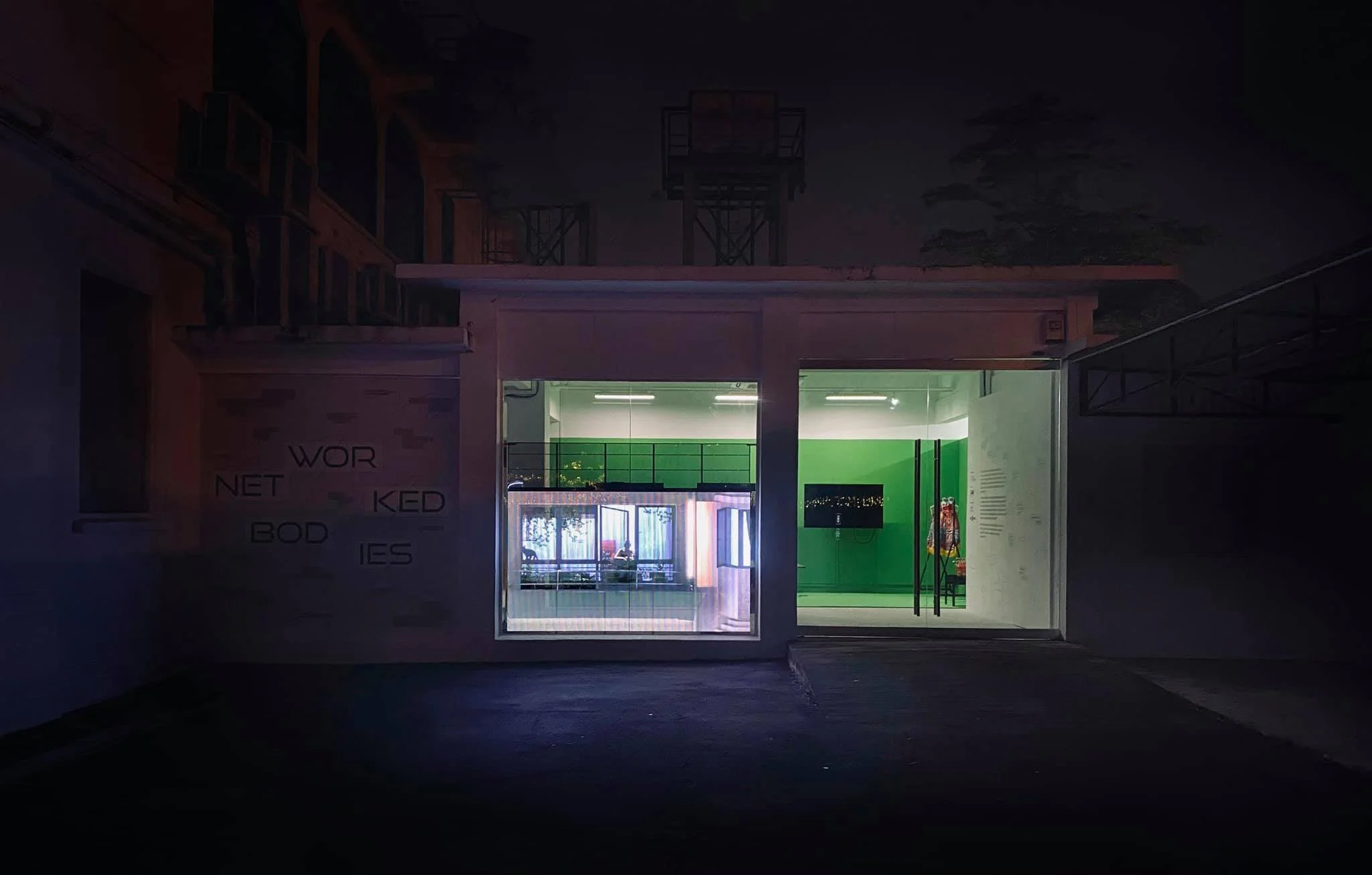 A building with a glass front illuminated from inside, showing a reception area with green walls and a TV on the wall.