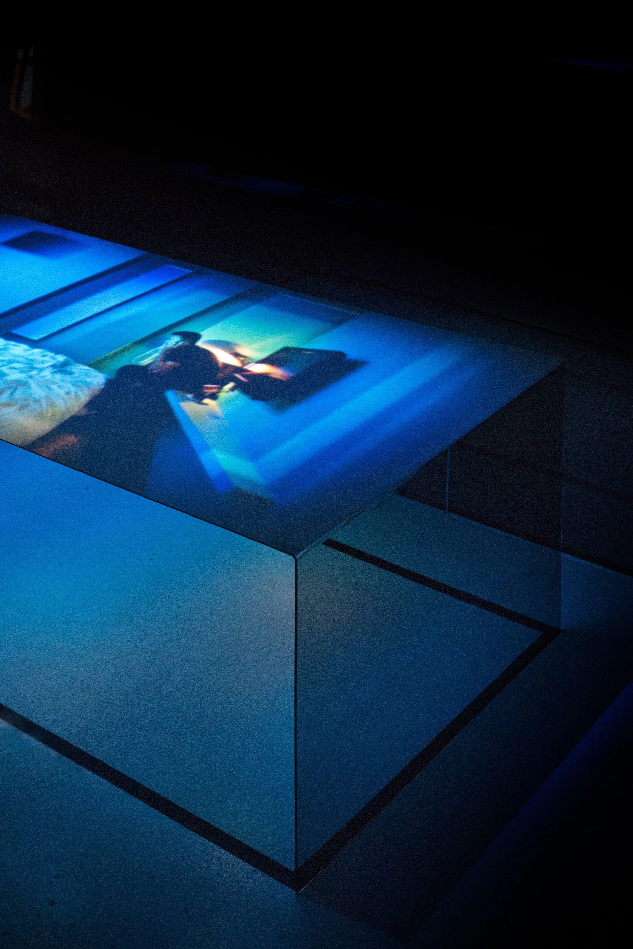A digital art piece projected onto a transparent glass surface, depicting a person sitting at a table with a colorful background.