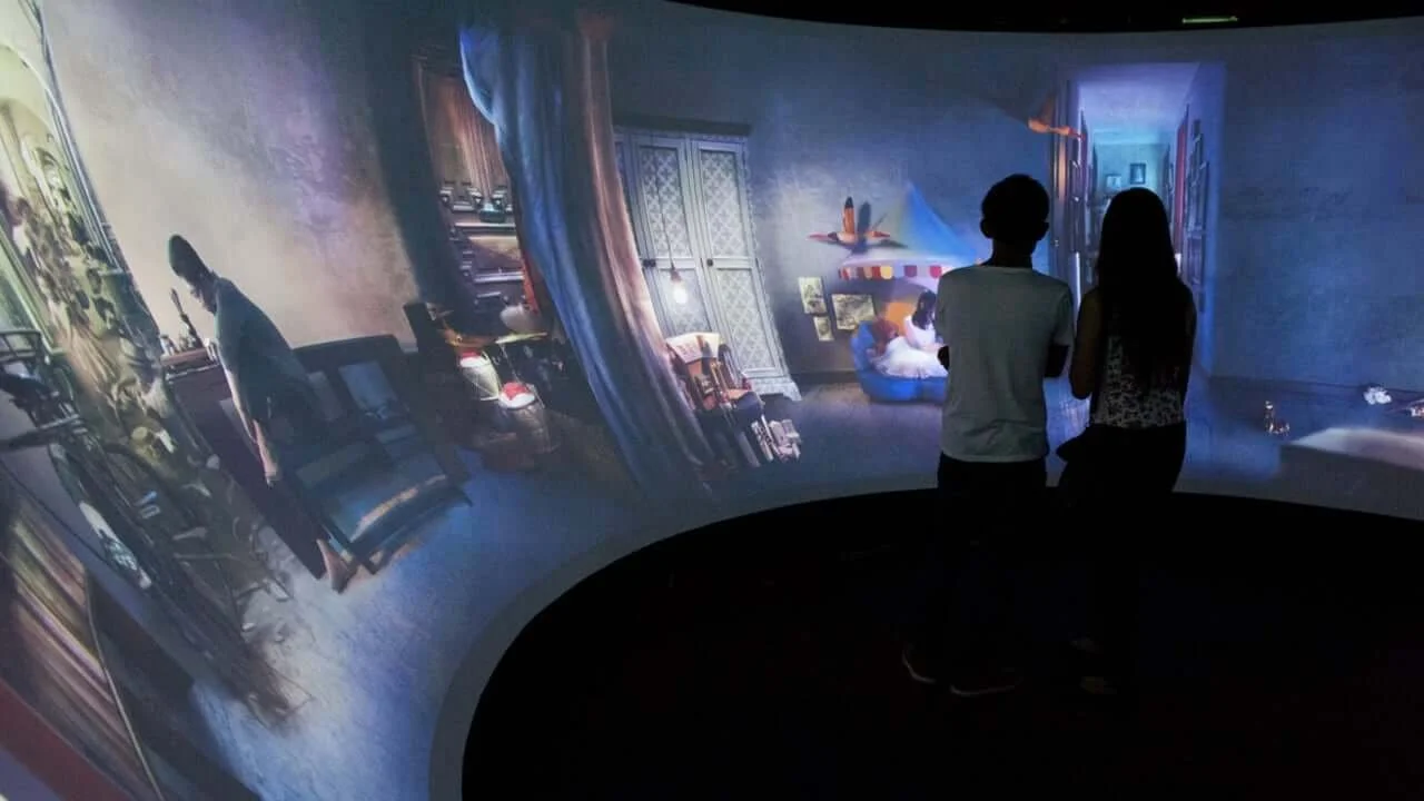 Two people standing inside an immersive, 3D projection of a children's bedroom with toys, books, and colorful decor.