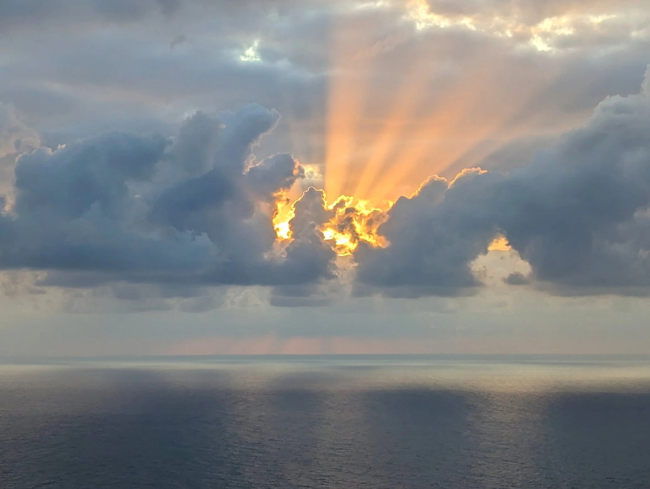 Sunset over the ocean with rays of sunlight peeking through dark clouds.