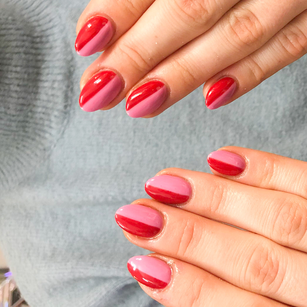 Close-up of a person's hands with manicured nails painted in pink and red gradient colors, resting on a light grey fabric.