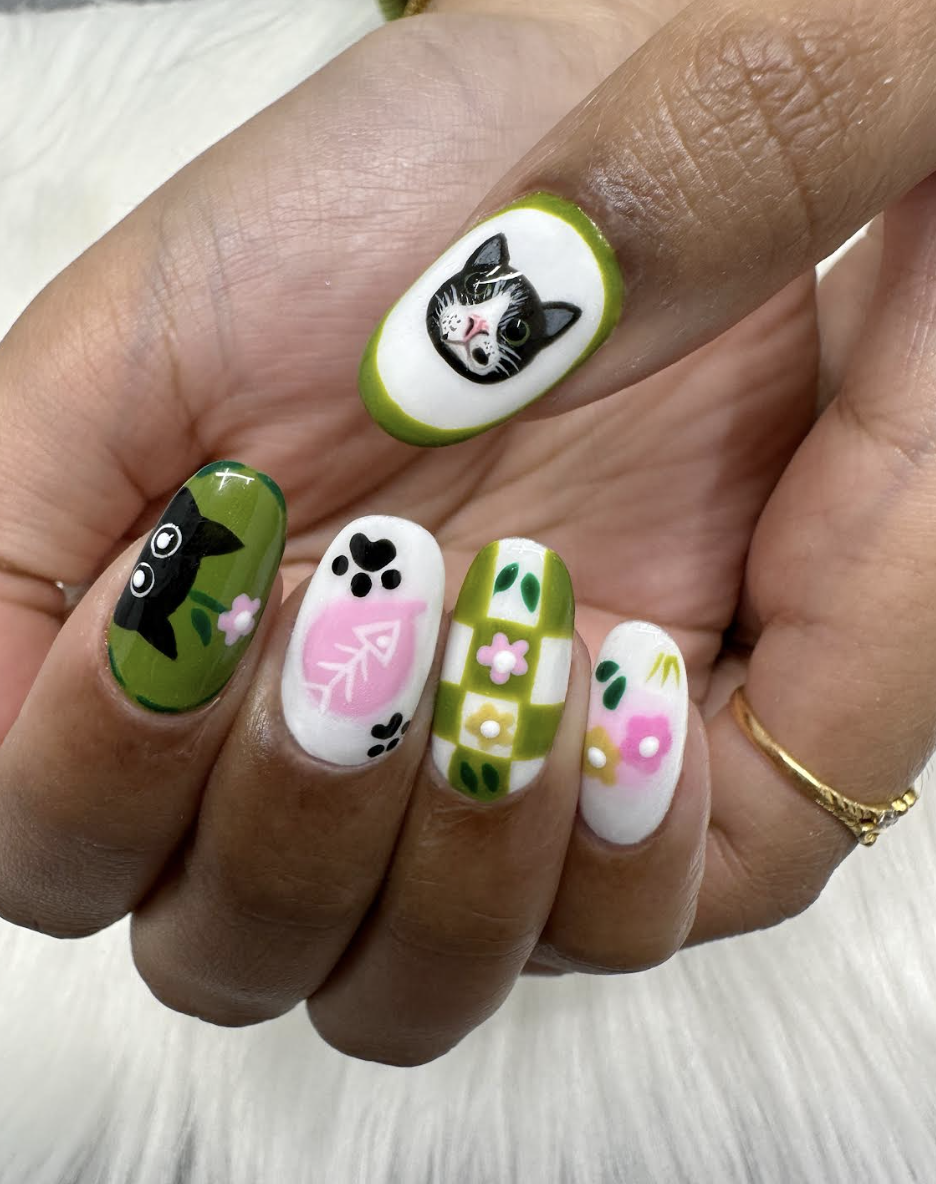 Nail art featuring cats, flowers, and leaf patterns in green, white, pink, and black colors.