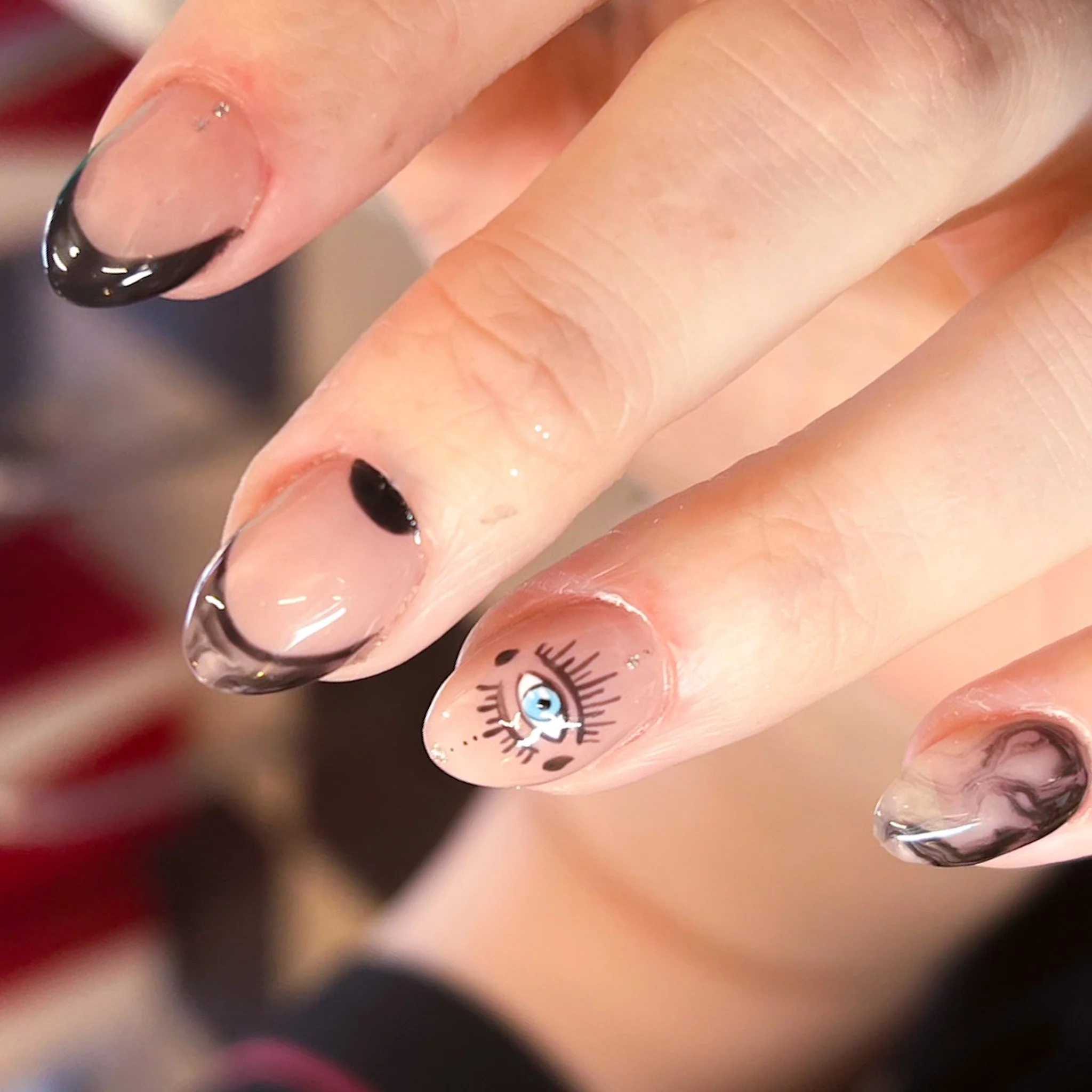 Close-up of a hand with decorated nail art, including a cute eye design on the ring finger, and black and clear marble effects on the other nails.
