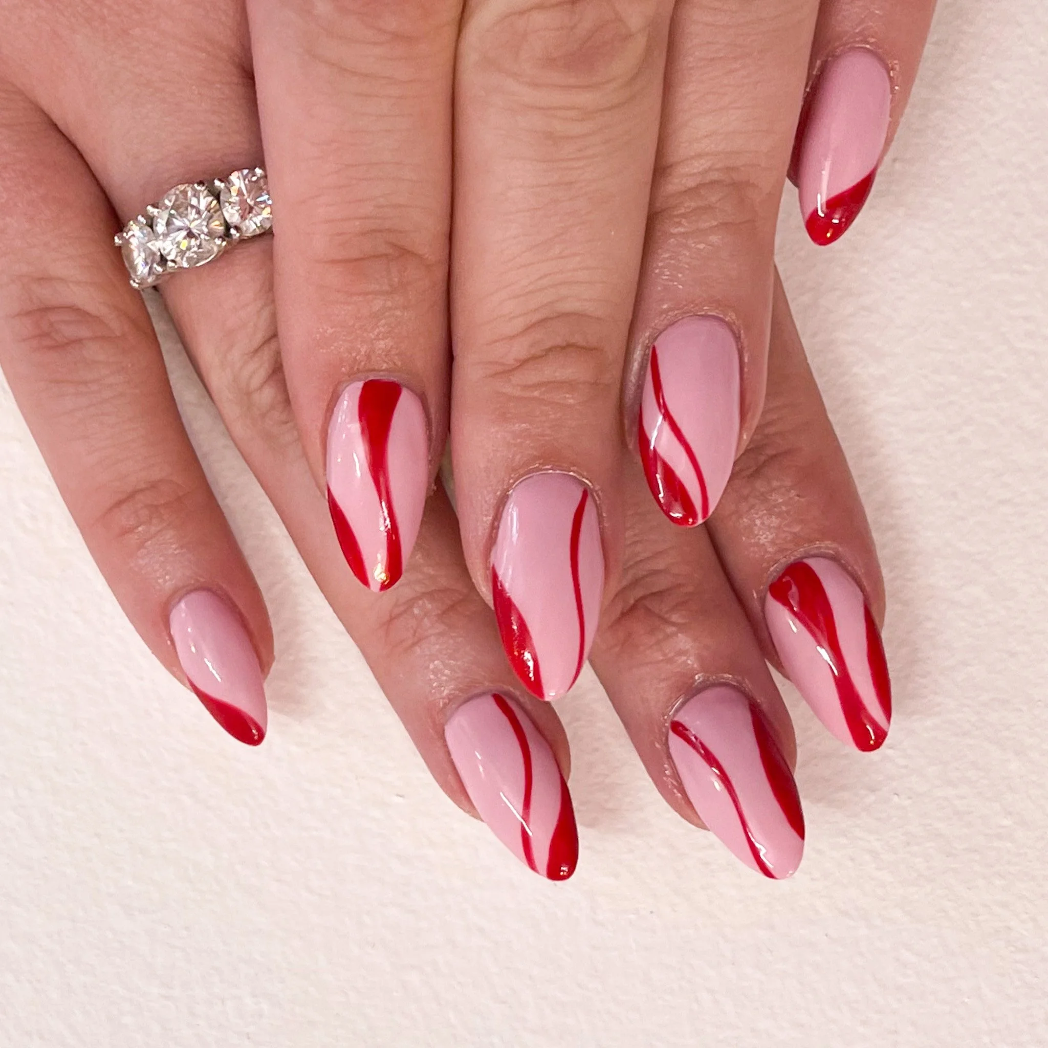 Close-up of a woman's hands with pink and red swirl nail art and a silver ring with multiple large clear gemstones.
