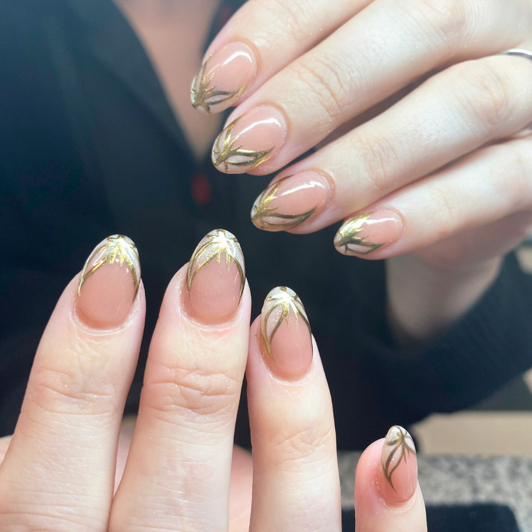 Close-up of hands showing metallic gold and black nail art designs on natural nails.