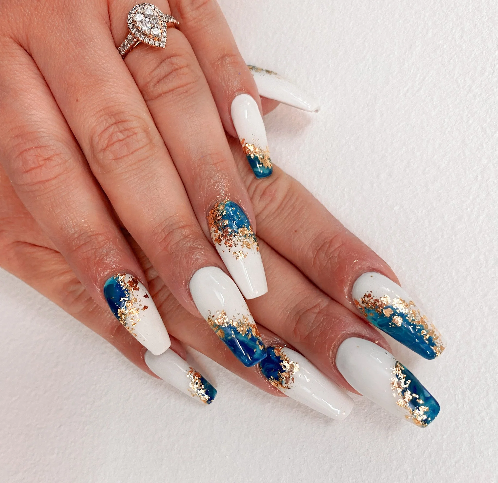 Close-up of a hand with elaborate white, blue, and gold glitter manicure and a silver ring with diamonds.