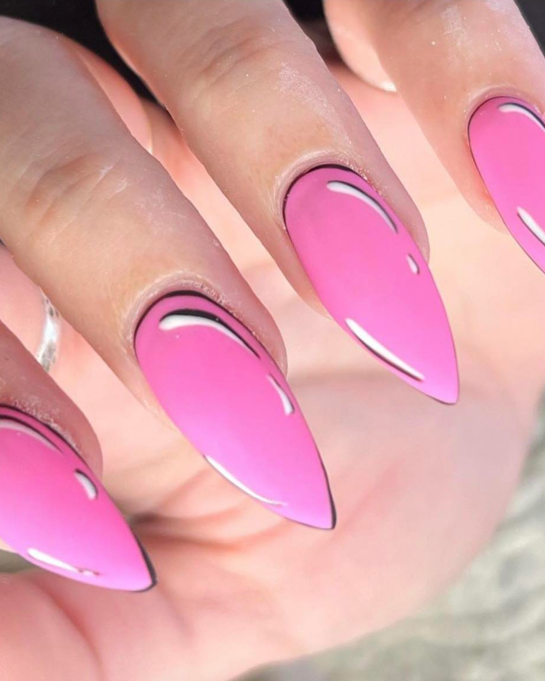 Close-up of a hand with nails painted in pink with black and white accents, shaped into long almond points.