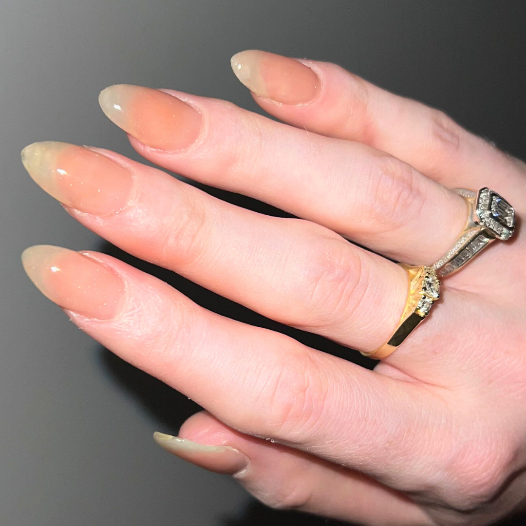 Close-up of a hand with manicured nails and two rings, one gold and one silver, on the ring finger.