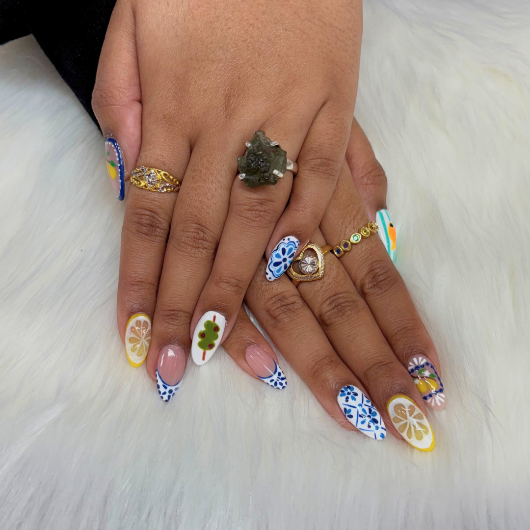Hand with colorful, patterned nails and multiple rings resting on a soft white surface.