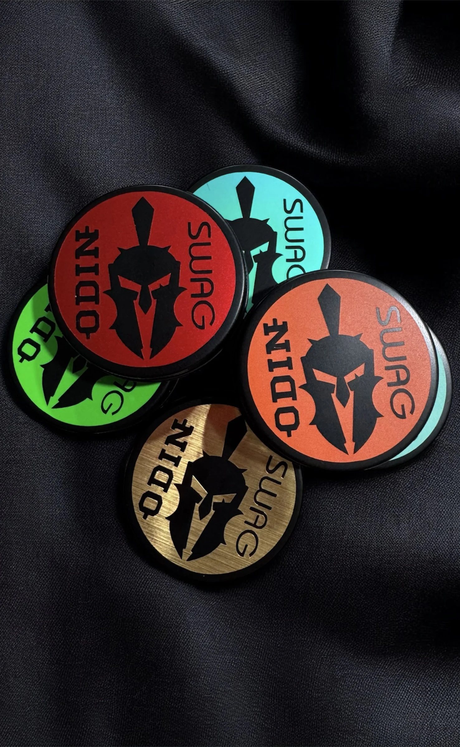 Colorful circular stickers with a black Spartan helmet logo and the text "DODIN G" on a black fabric background.