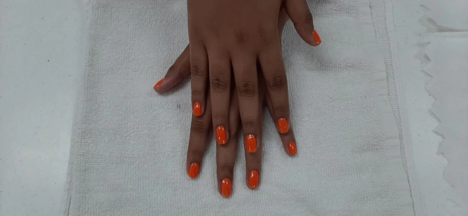 A person's hand with orange-painted nails resting on a white surface.