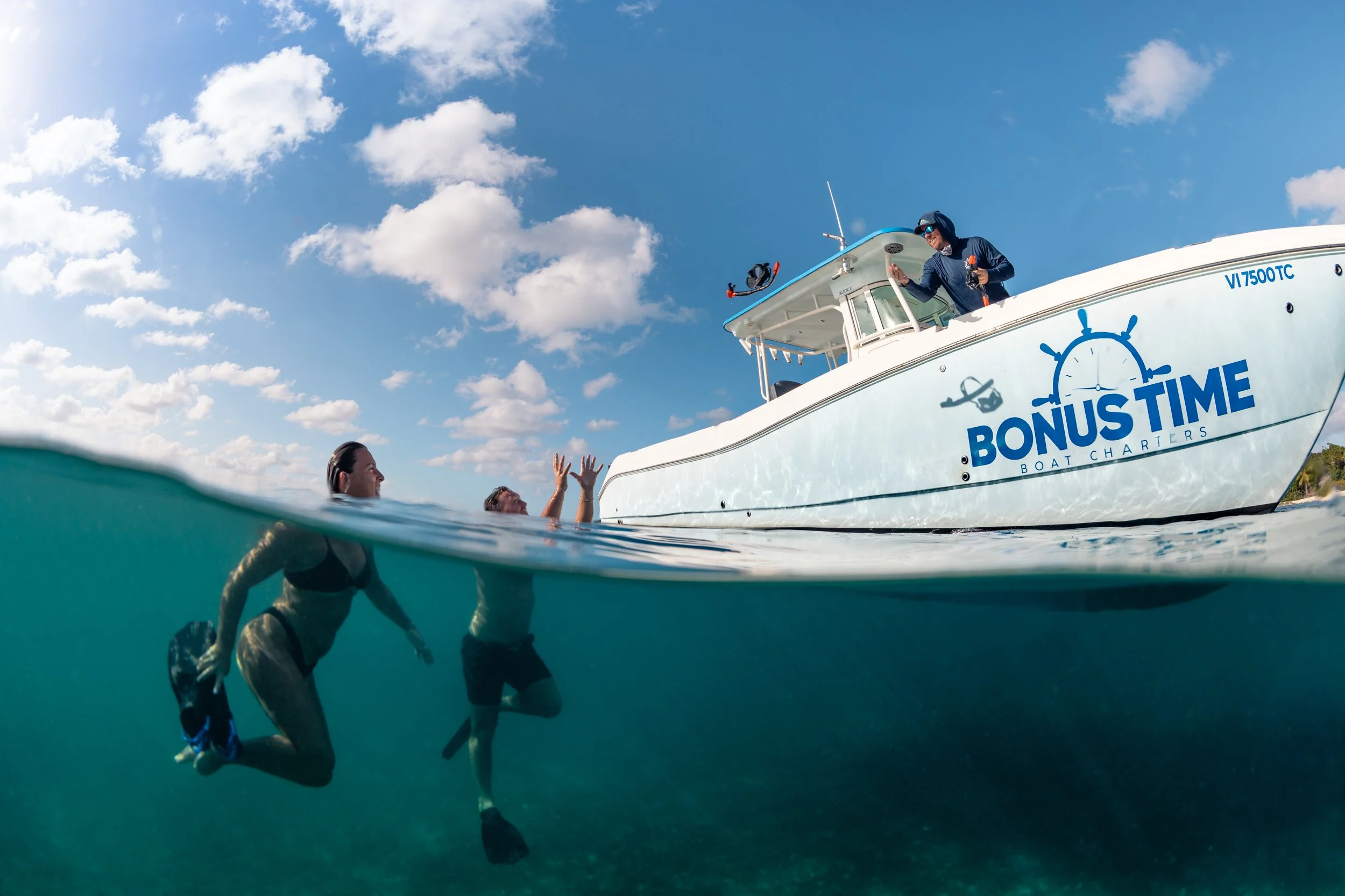 People swimming near a white boat with the logo "Bonus Time Boat Charters" on the side. Two women are underwater, and one man is struggling to reach the boat. A man on the boat is holding a hand out to help.