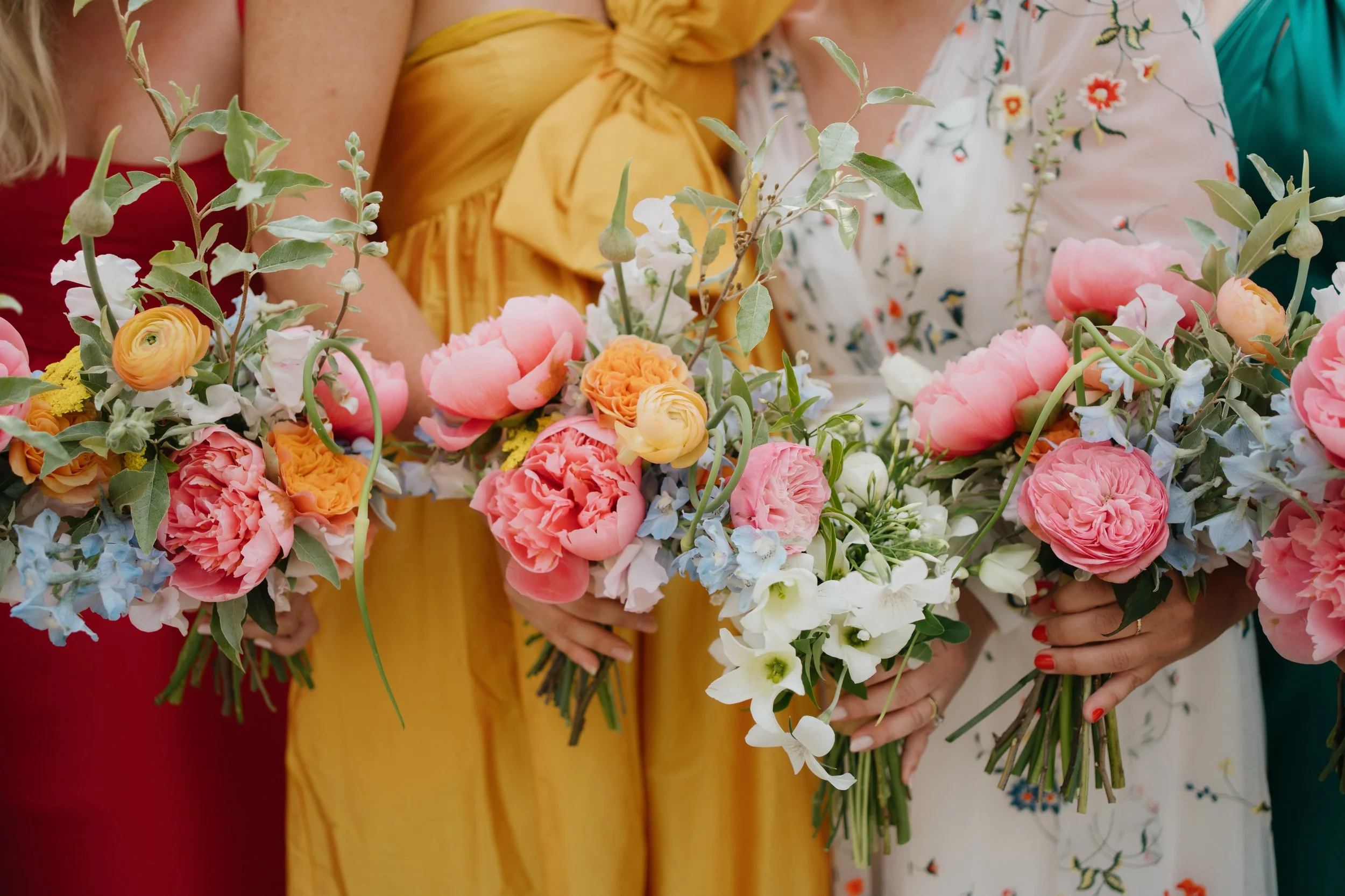 People holding flower bouquets with pink, white, orange, and blue flowers.