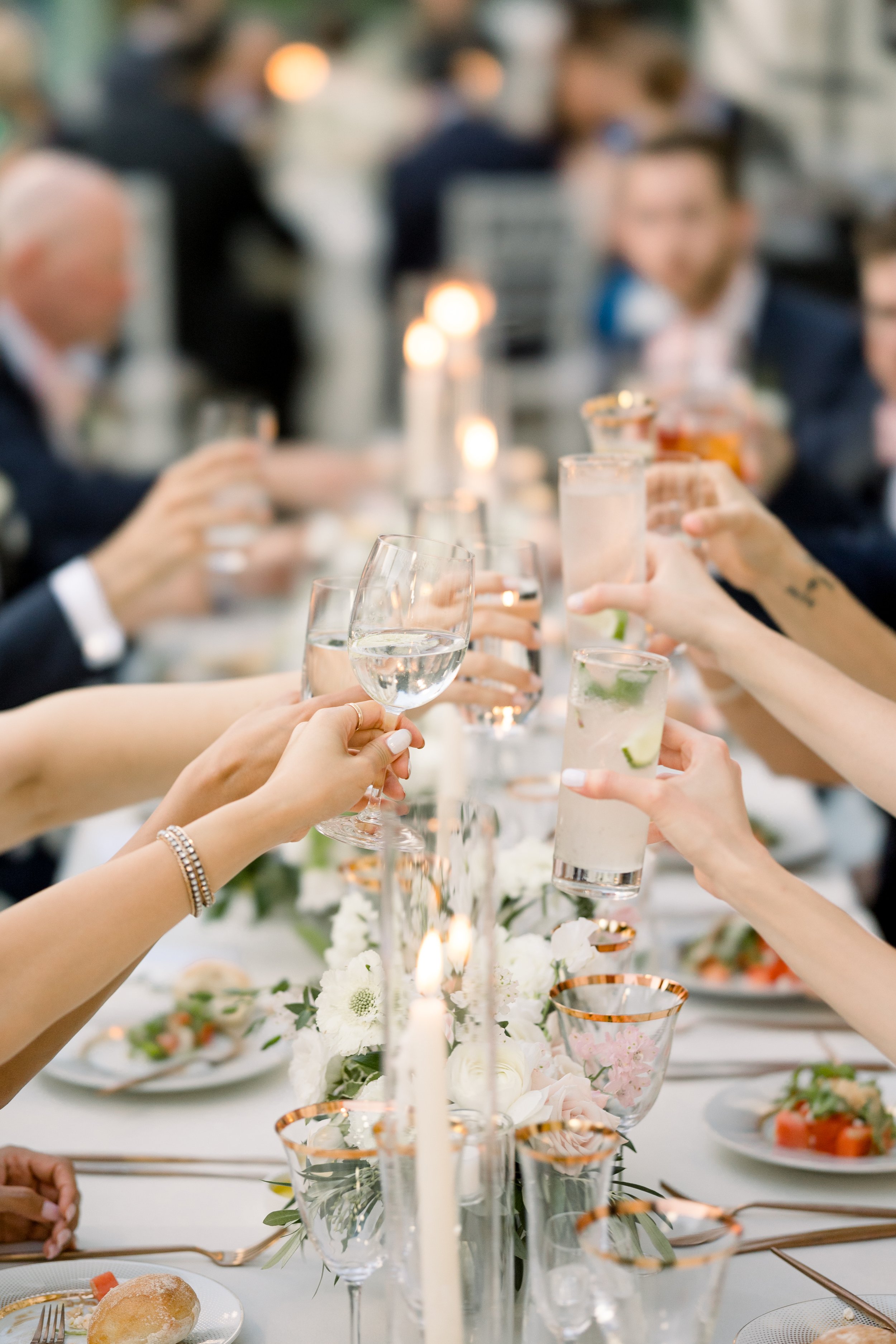 People raising glasses at a formal dinner party with candles, flowers, and elegant tableware.