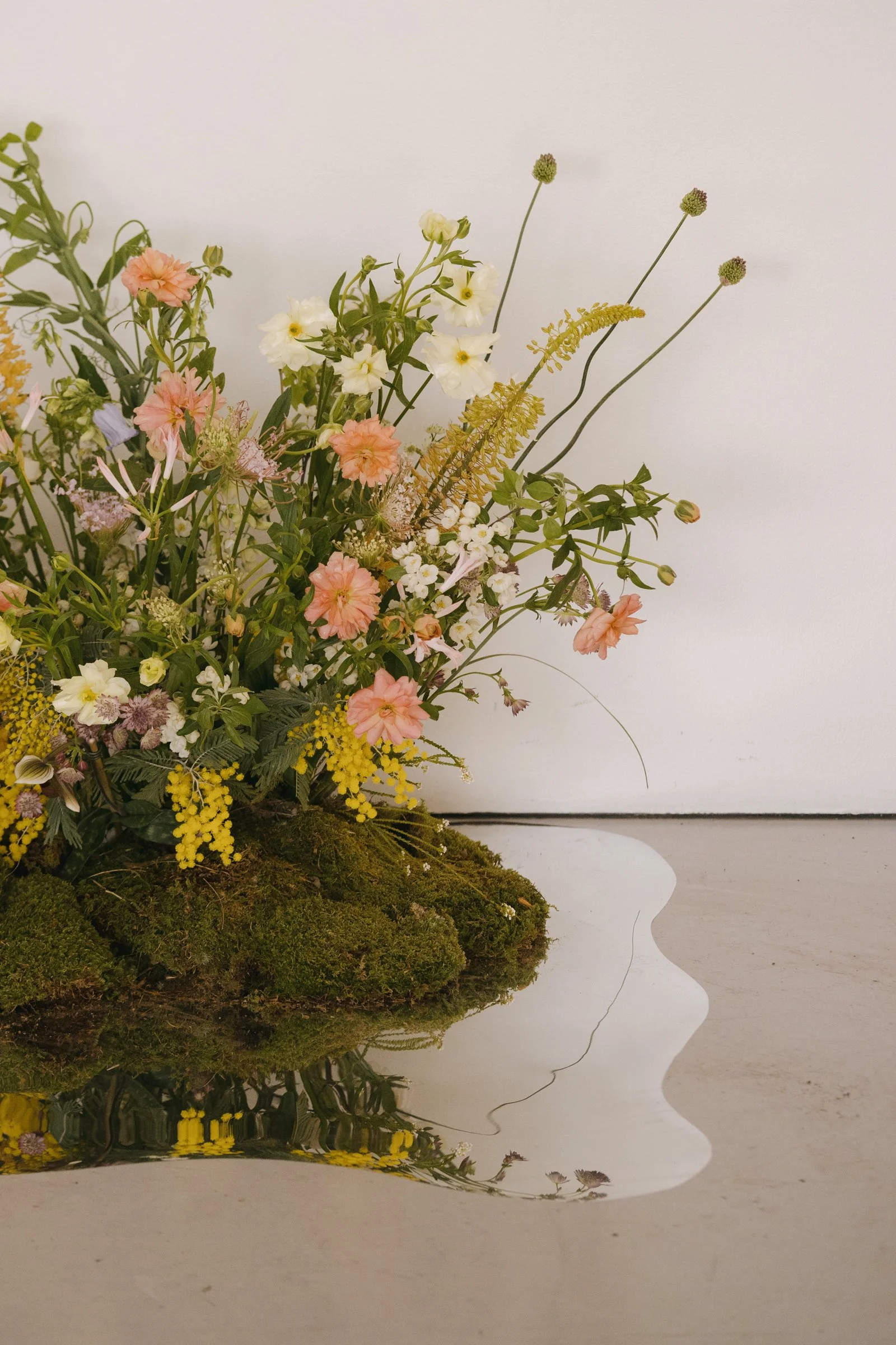 Flowers arrangement with pink, white, and yellow blossoms, reflected on a shiny surface, against a plain white background.