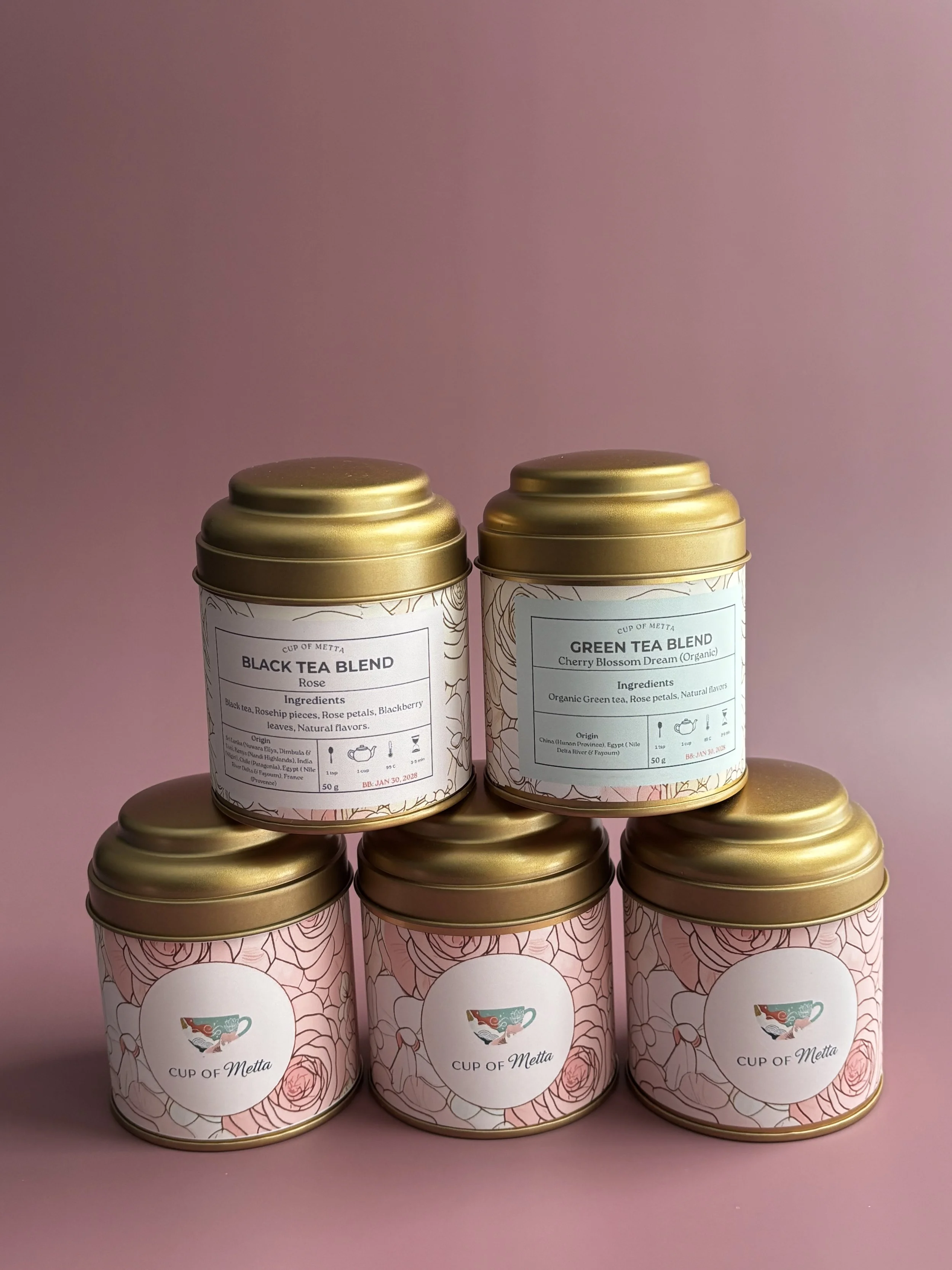 Six tins of tea with pink floral labels and gold lids, arranged in two rows against a pink background.