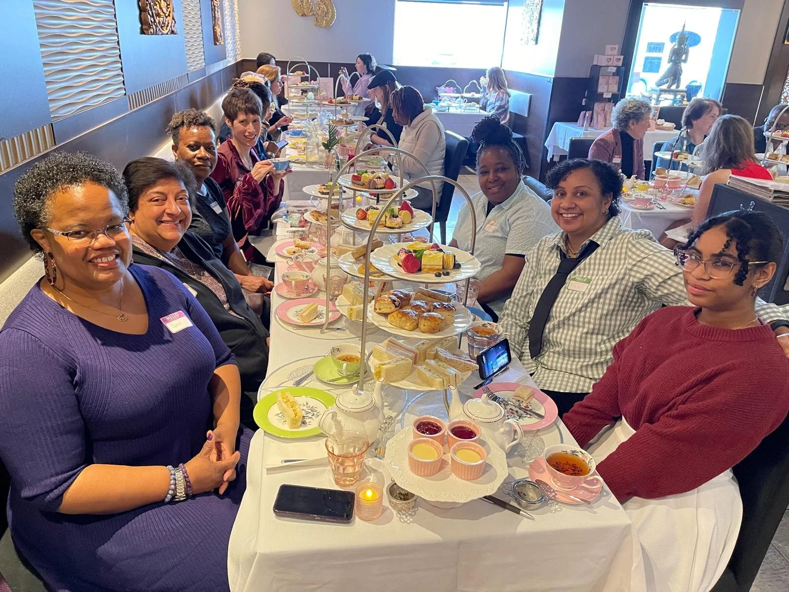 Group of women having afternoon tea at a restaurant with various pastries, cakes, and tea cups on the table.