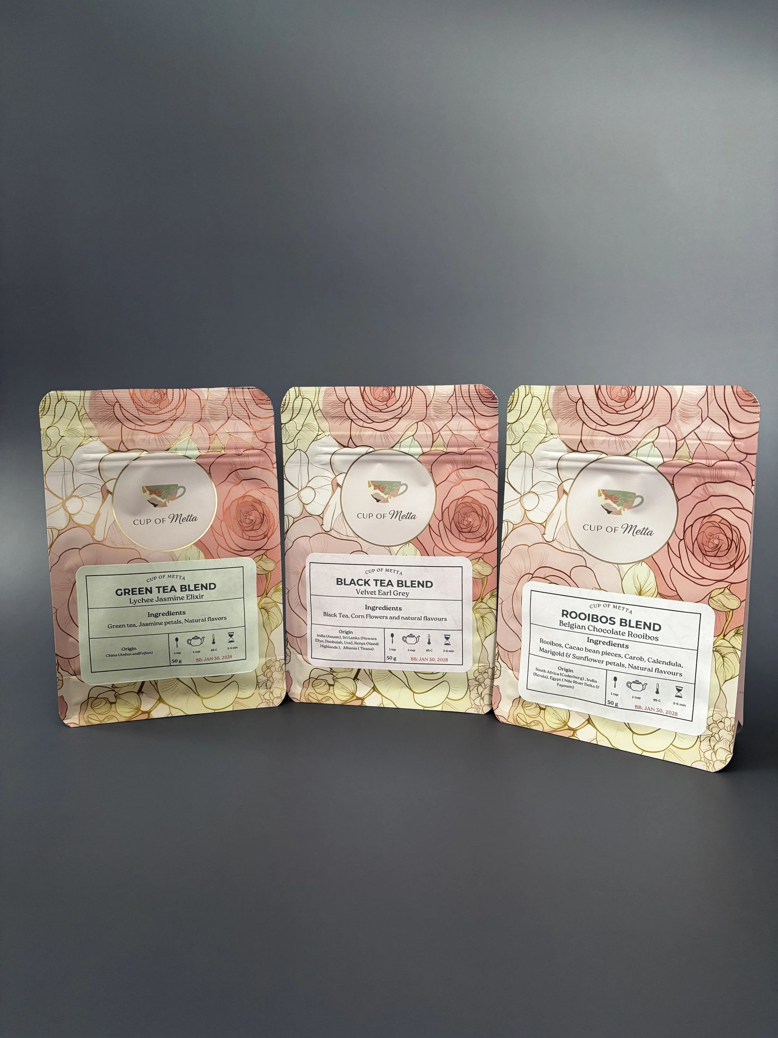 Three packages of tea blends labeled Green Tea Blend, Black Tea Blend, and Rooibos Blend, with floral and leaf designs on pink backgrounds.