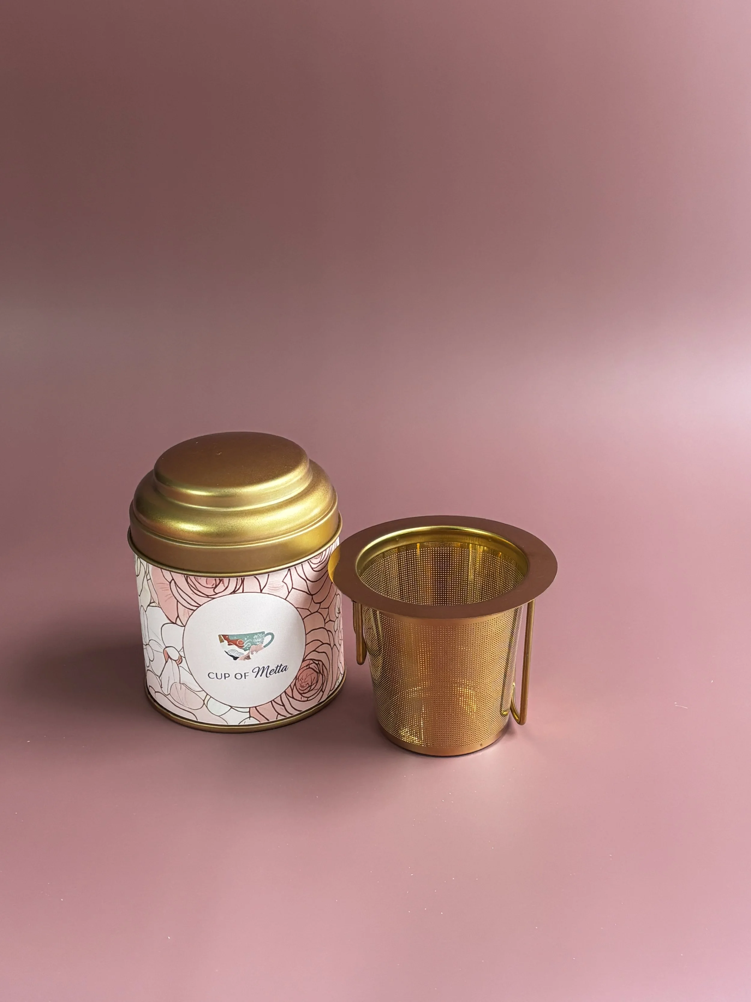 A tea infuser and a decorative container with a label that says 'Cup of Metta' on a pink background.
