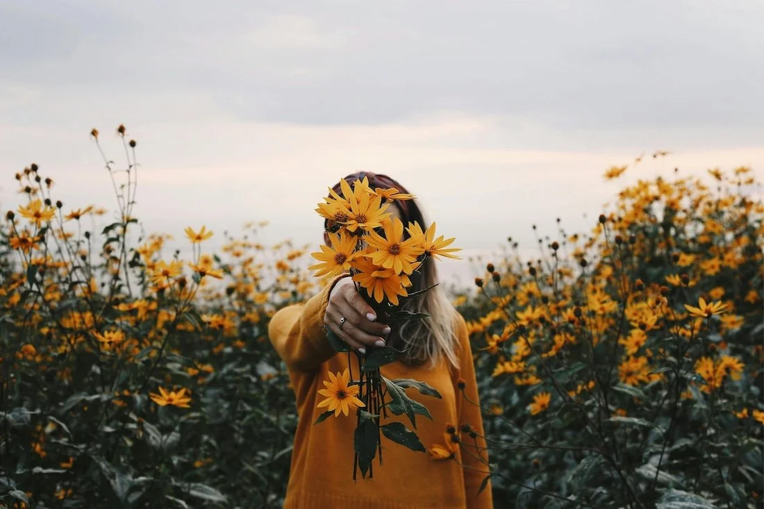 womans health naturopath yeppoon -  holding a bouquet of yellow flowers in front of their face in a field of yellow flowers.