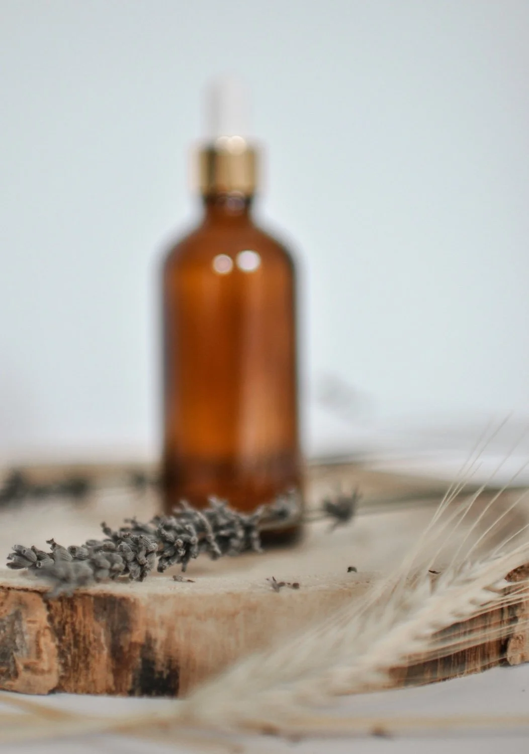 Herbal medicine for natural health yeppoon A blurred amber glass bottle with a white dropper cap, placed on a wooden surface with dried lavender and wheat stalks.