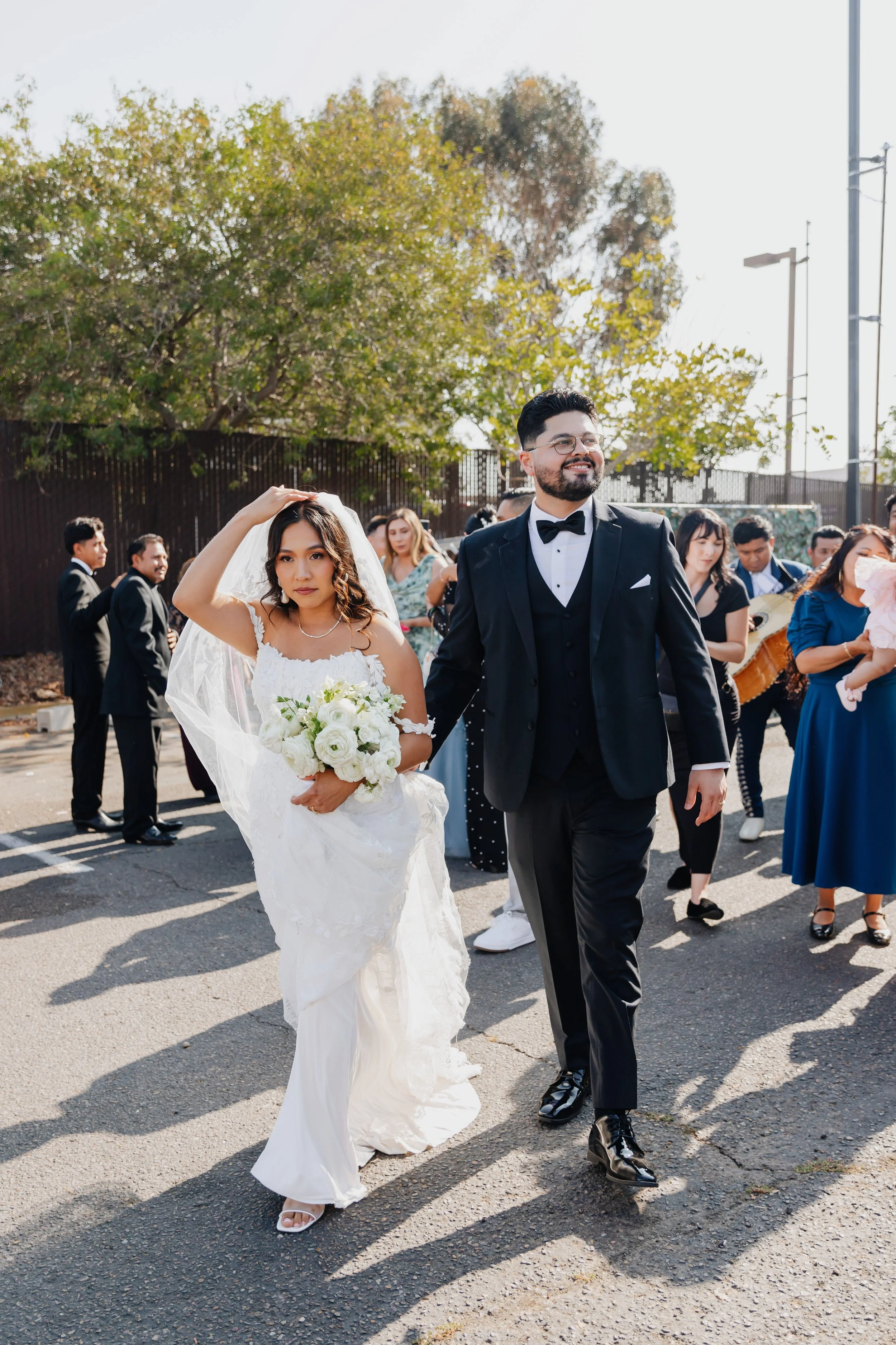 A woman in a black and red floral dress and black hat standing beside a gray horse in a wooded area with tall trees and fallen leaves.