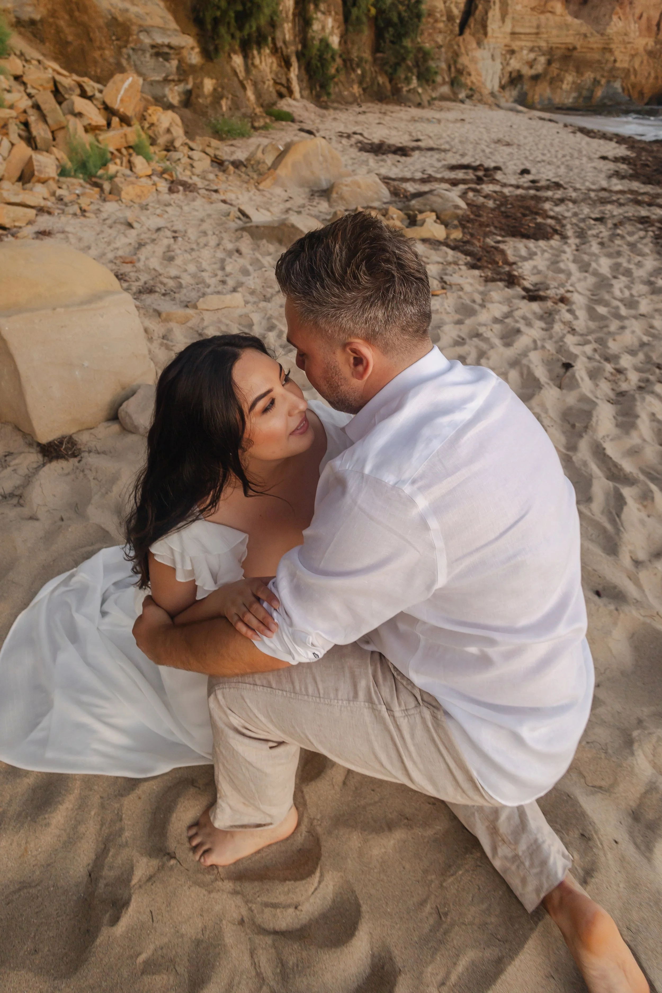 A woman in an elaborate champagne-colored gown with gold embellishments, wearing a tiara, standing outdoors on a columned porch with a white building in the background.