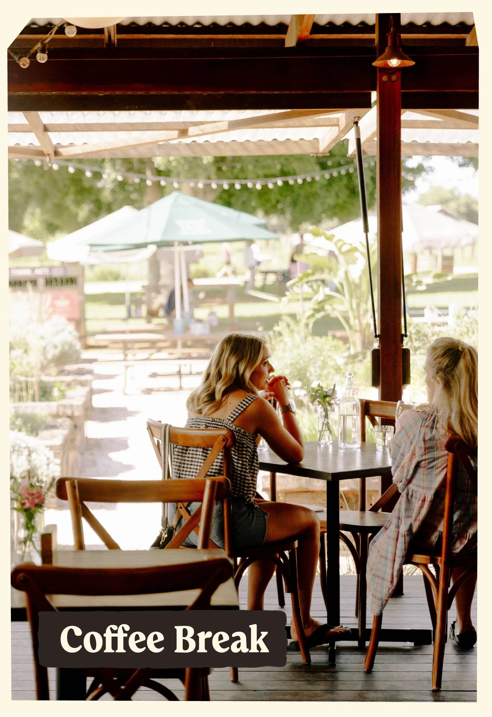 Two women sit across from each other at a table inside a cafe during daytime, with a sign reading 'Coffee Break' at the bottom, and outdoor greenery visible through the open window.