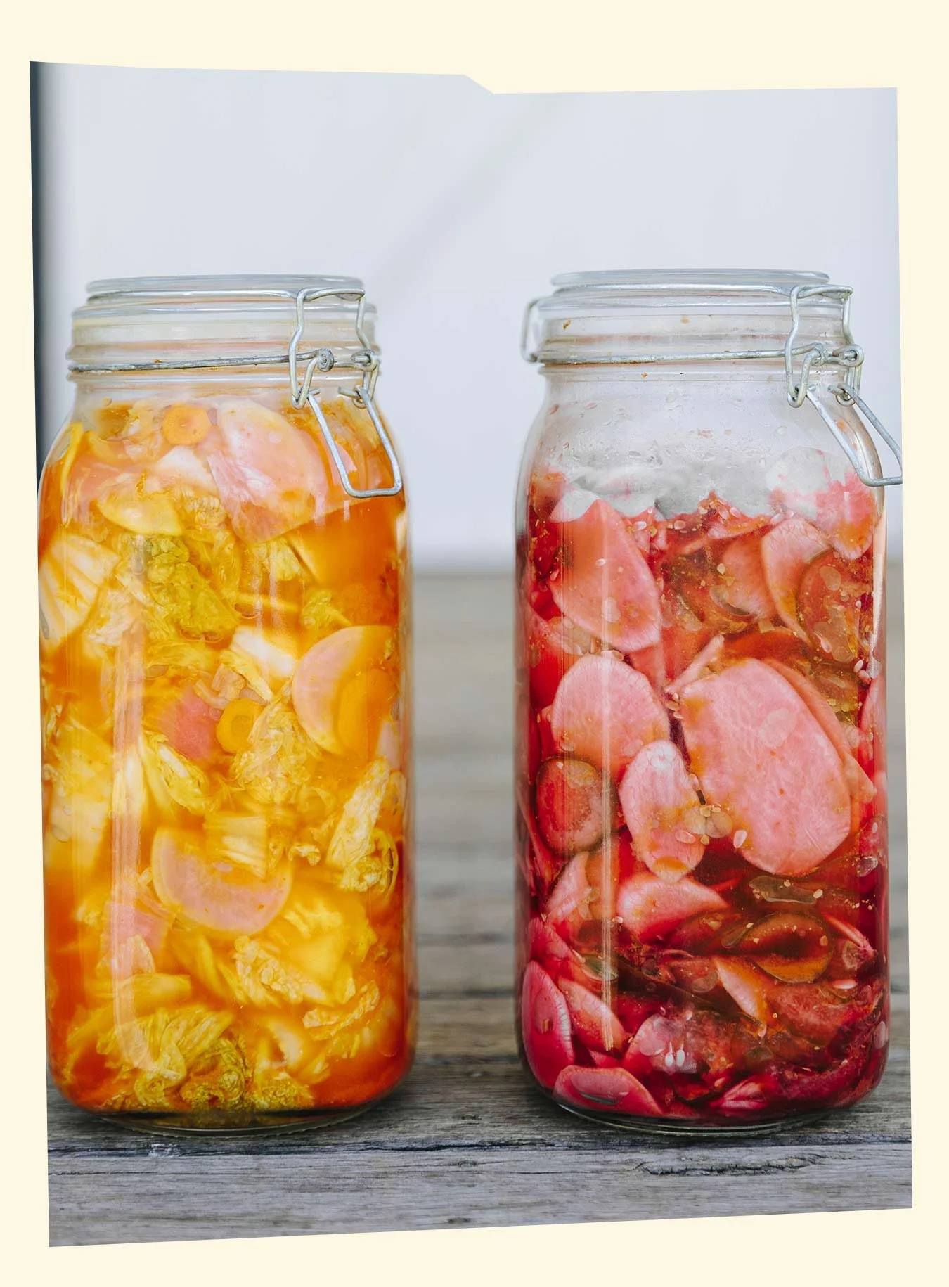 Two glass jars filled with pickled vegetables, one with yellow-colored vegetables and the other with red-colored vegetables, placed on a wooden surface.