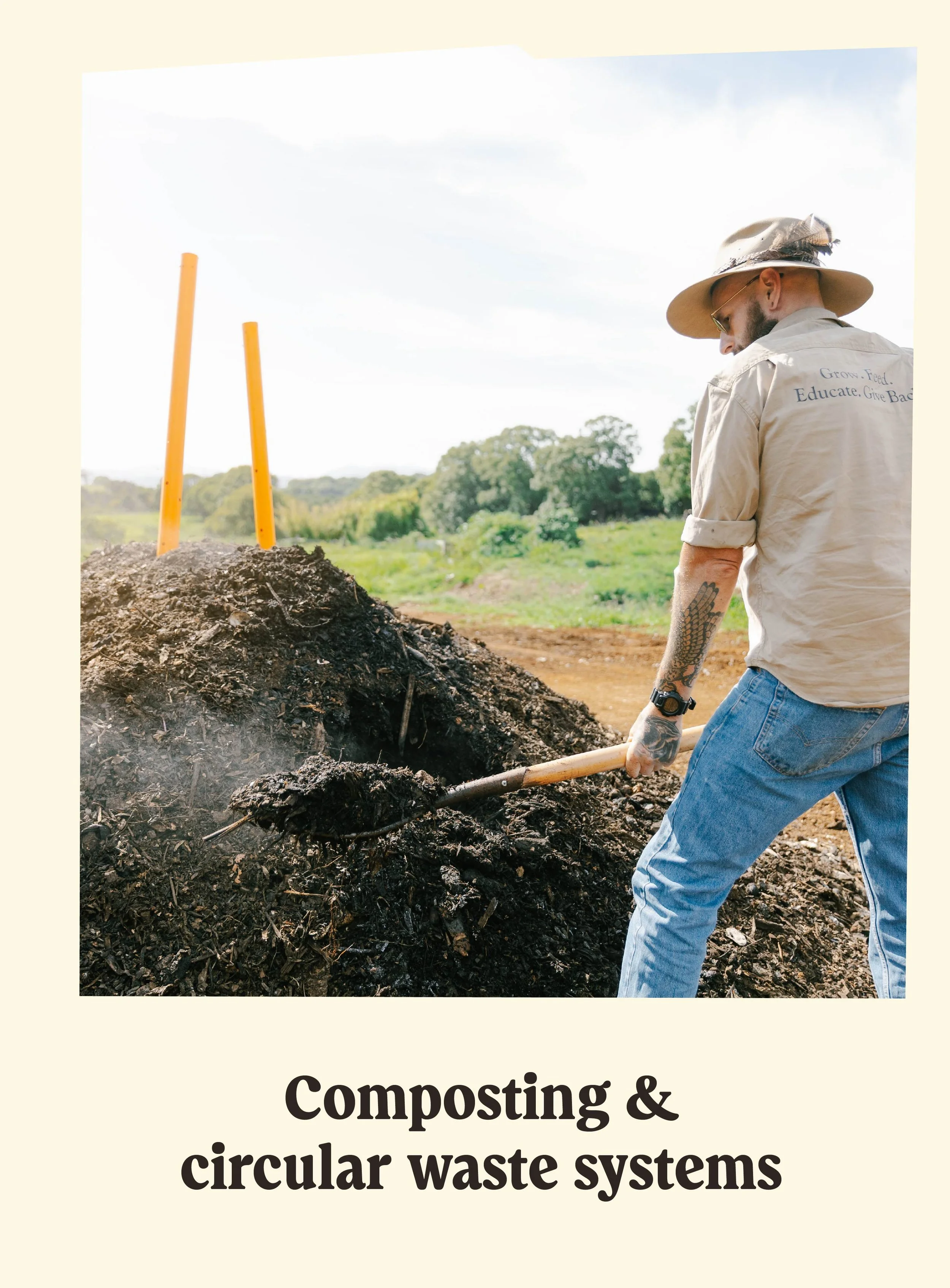 A man in a beige shirt and wide-brimmed hat shovels compost or organic material into a pile outdoors, with trees and a blue sky in the background.
