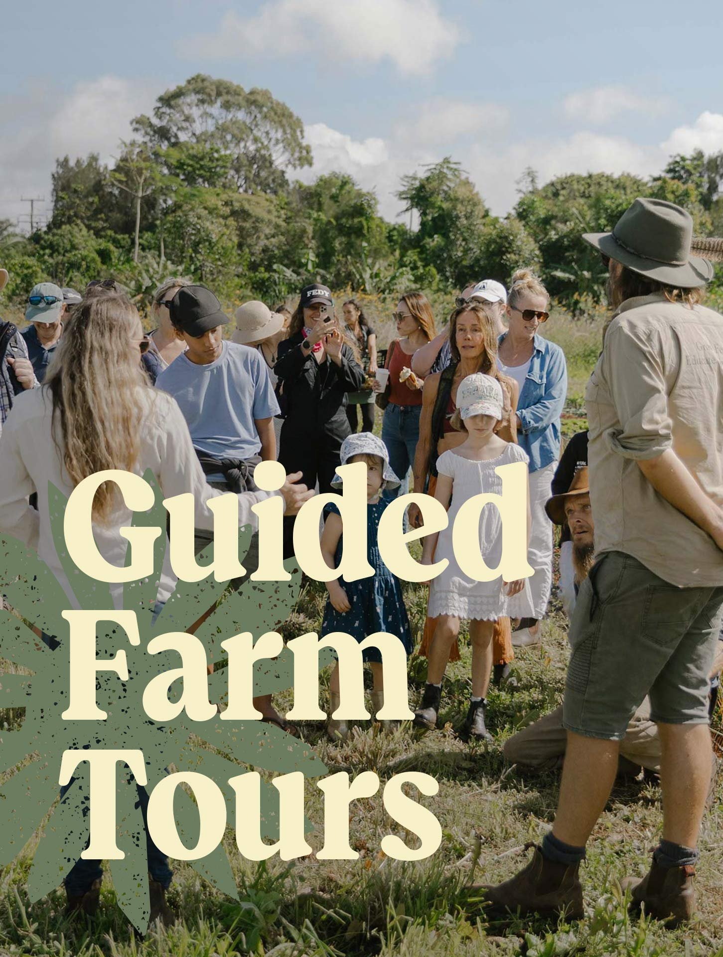 A group of people on a farm tour in a field with greenery and trees, some taking photos, listening to a guide, and wearing casual outdoor clothing and hats.