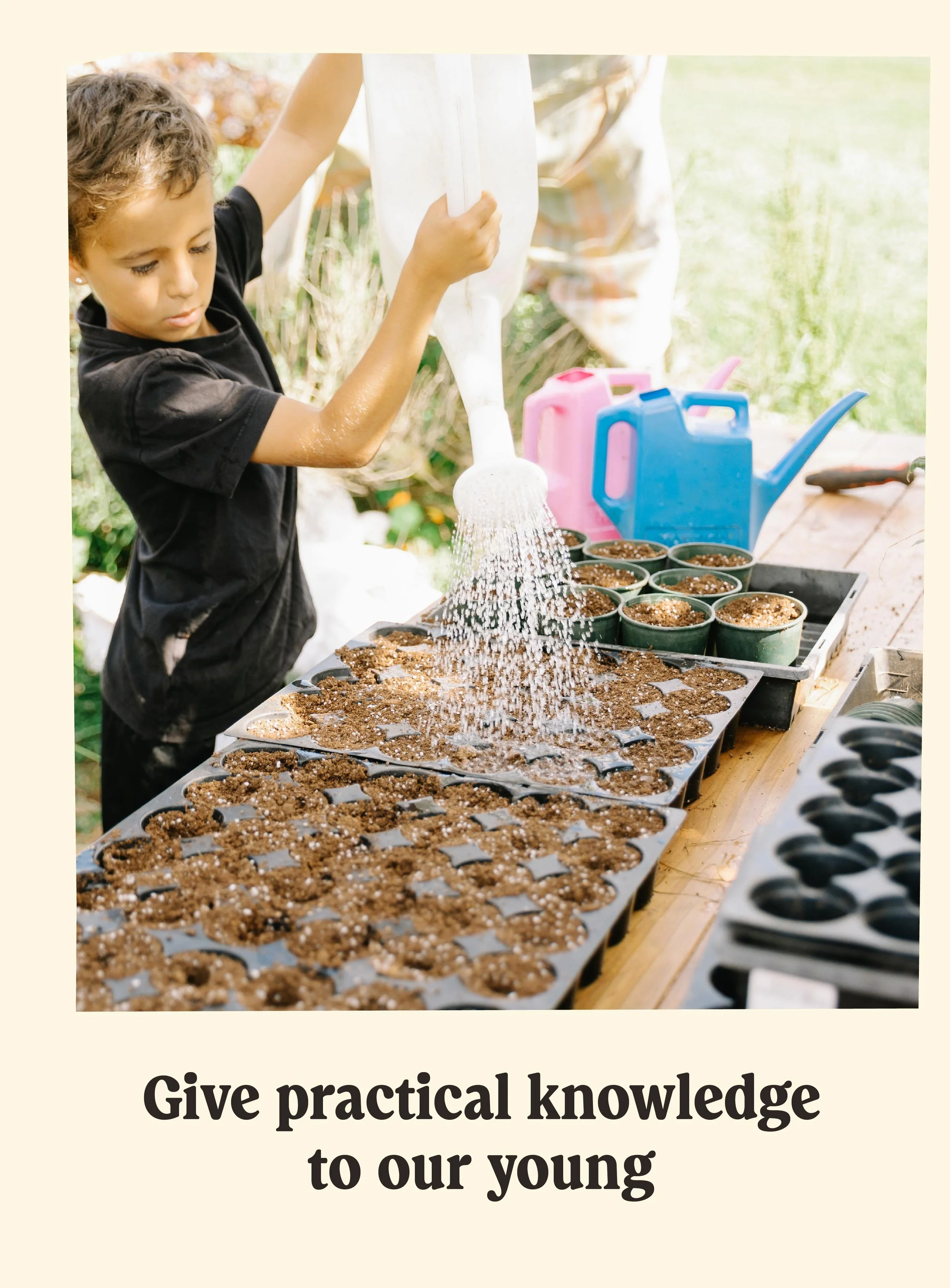 A young girl watering small soil-filled pots on a wooden table outdoors, with gardening supplies in background, including water cans.