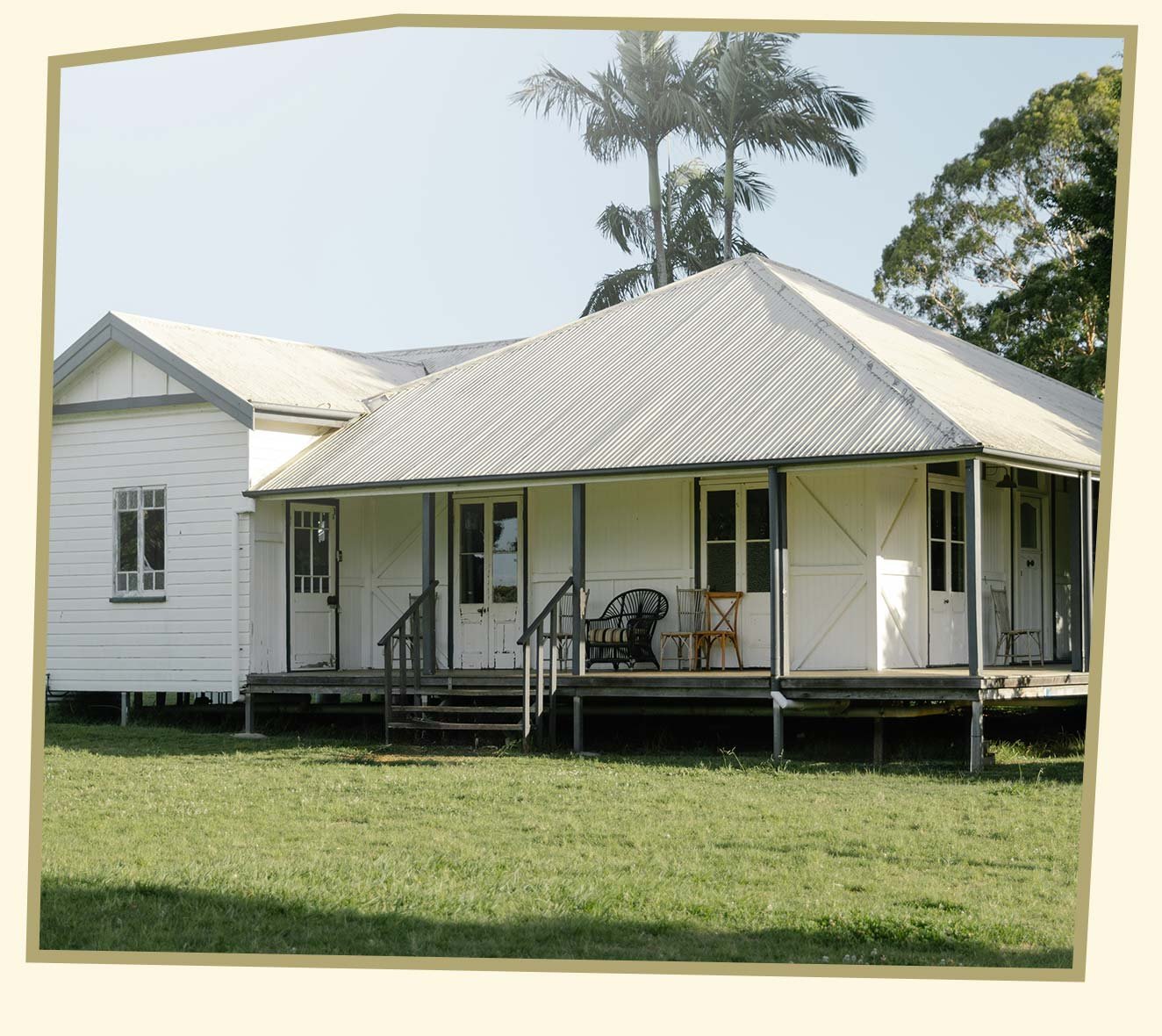 A white house with a porch supported by dark blue columns, set on a grassy lawn with trees in the background.