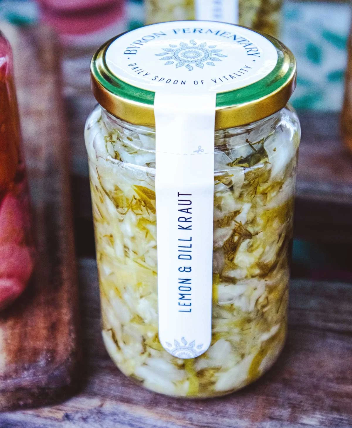 Jar labeled 'Lemon & Dill Kraut' containing fermented cabbage with lemon slices and dill, on a wooden surface.